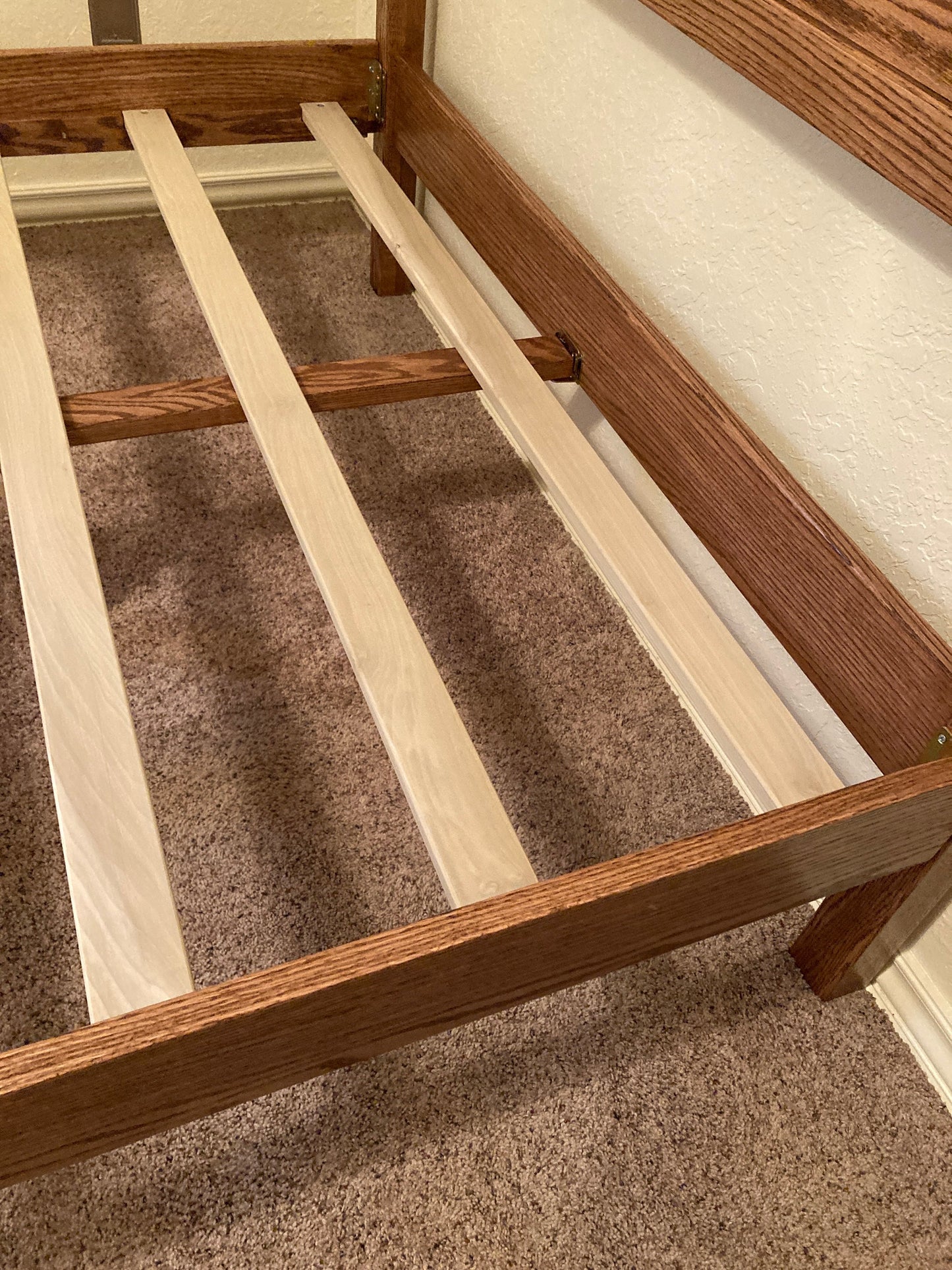A wooden oak bed frame with a light brown stain. The frame has a slatted support system with poplar slats. The frame is sitting on a brown carpet.