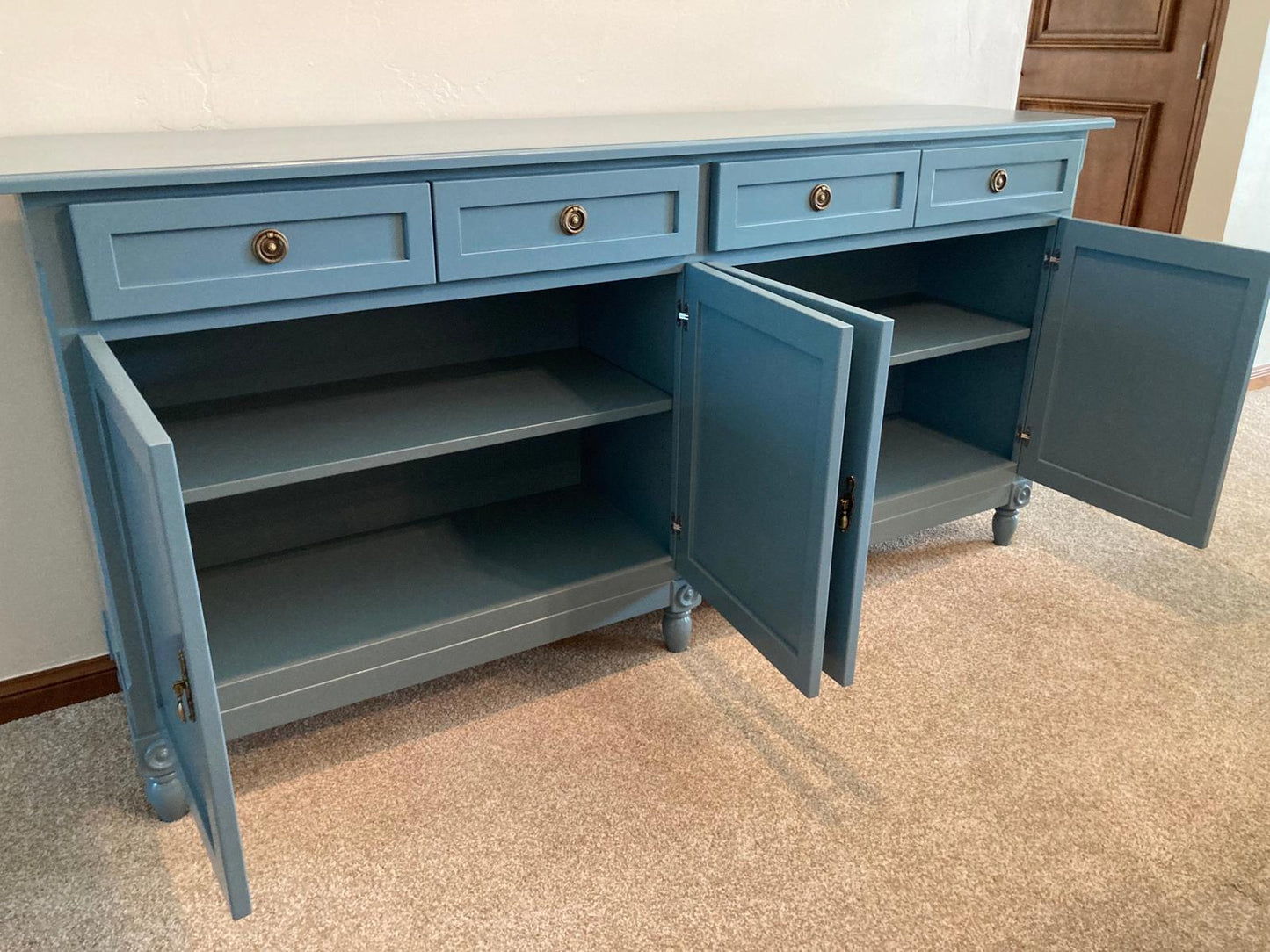 A blue wooden cabinet with four drawers and four doors. The doors are open and reveal shelves inside. The cabinet has decorative legs and brass knobs.