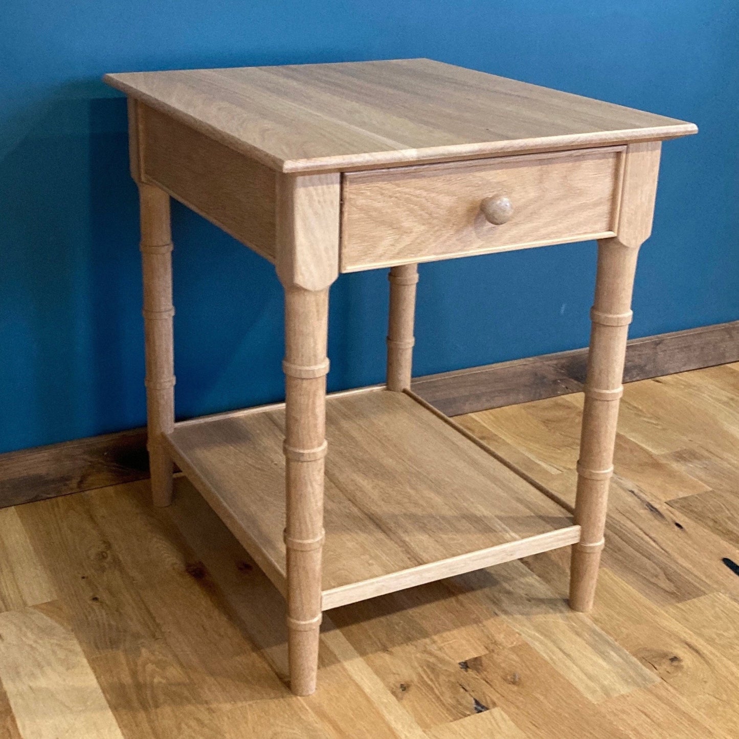 A light wood end table with a single drawer and a lower shelf. The table has turned faux bamboo legs and a simple design.