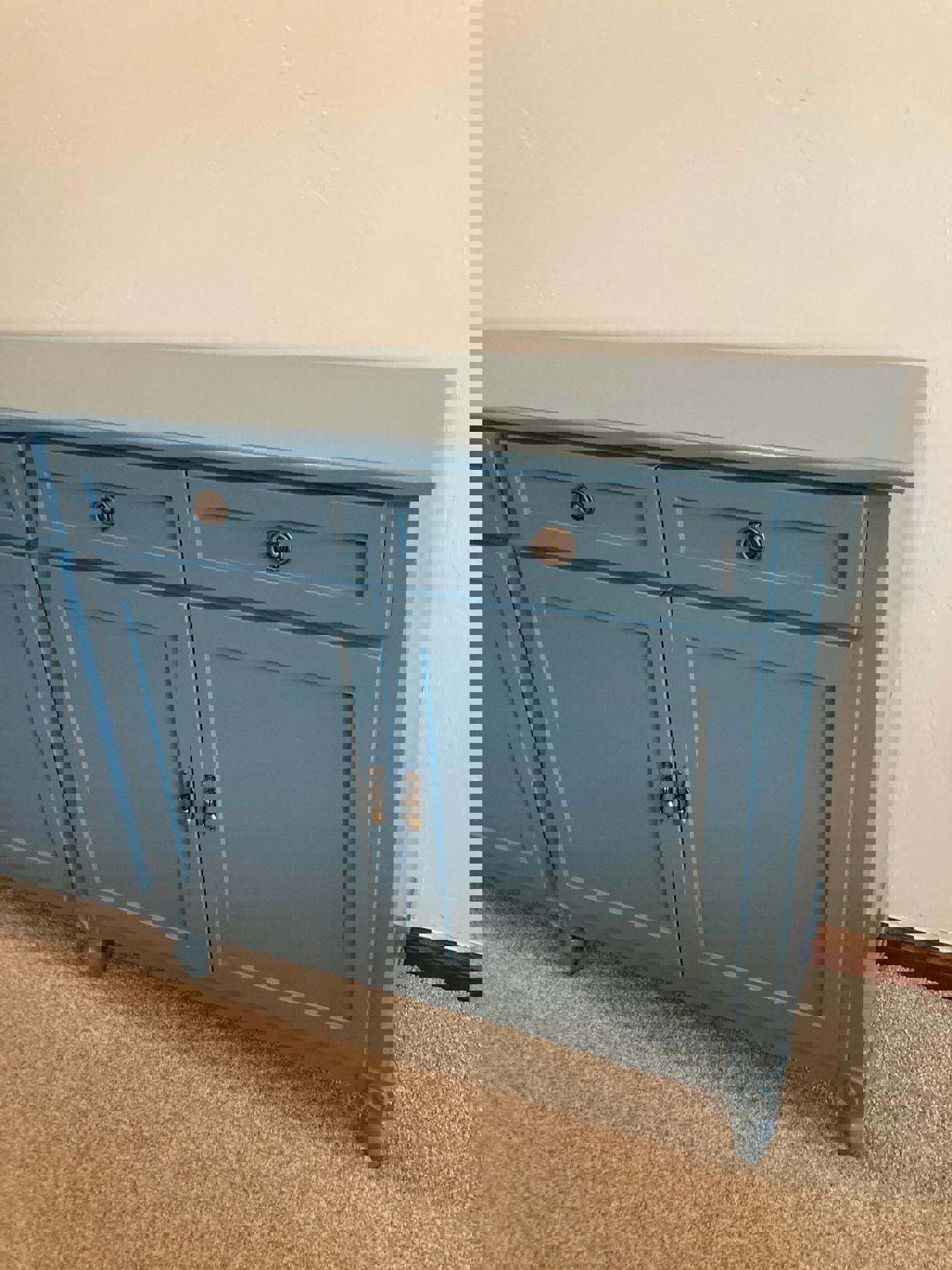 The right side of a light blue wooden cabinets four doors and two drawers. The cabinet has brass knobs and sits on four legs. The cabinet is on a light brown carpet.