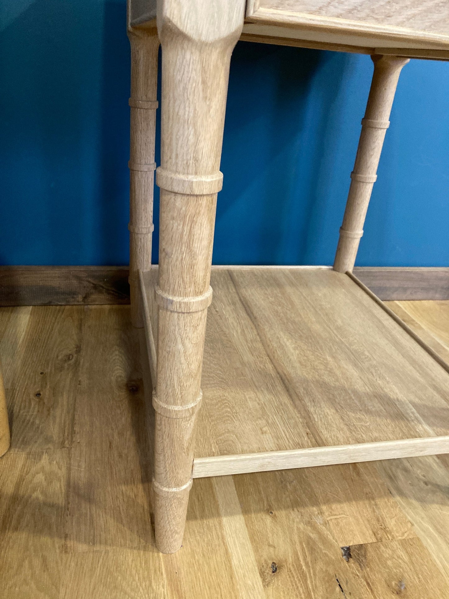 Close-up of a light wood end table with a single drawer and a lower shelf. The table has a simple design with turned faux bamboo legs and a rectangular top. The table is made of light wood and has a natural finish.