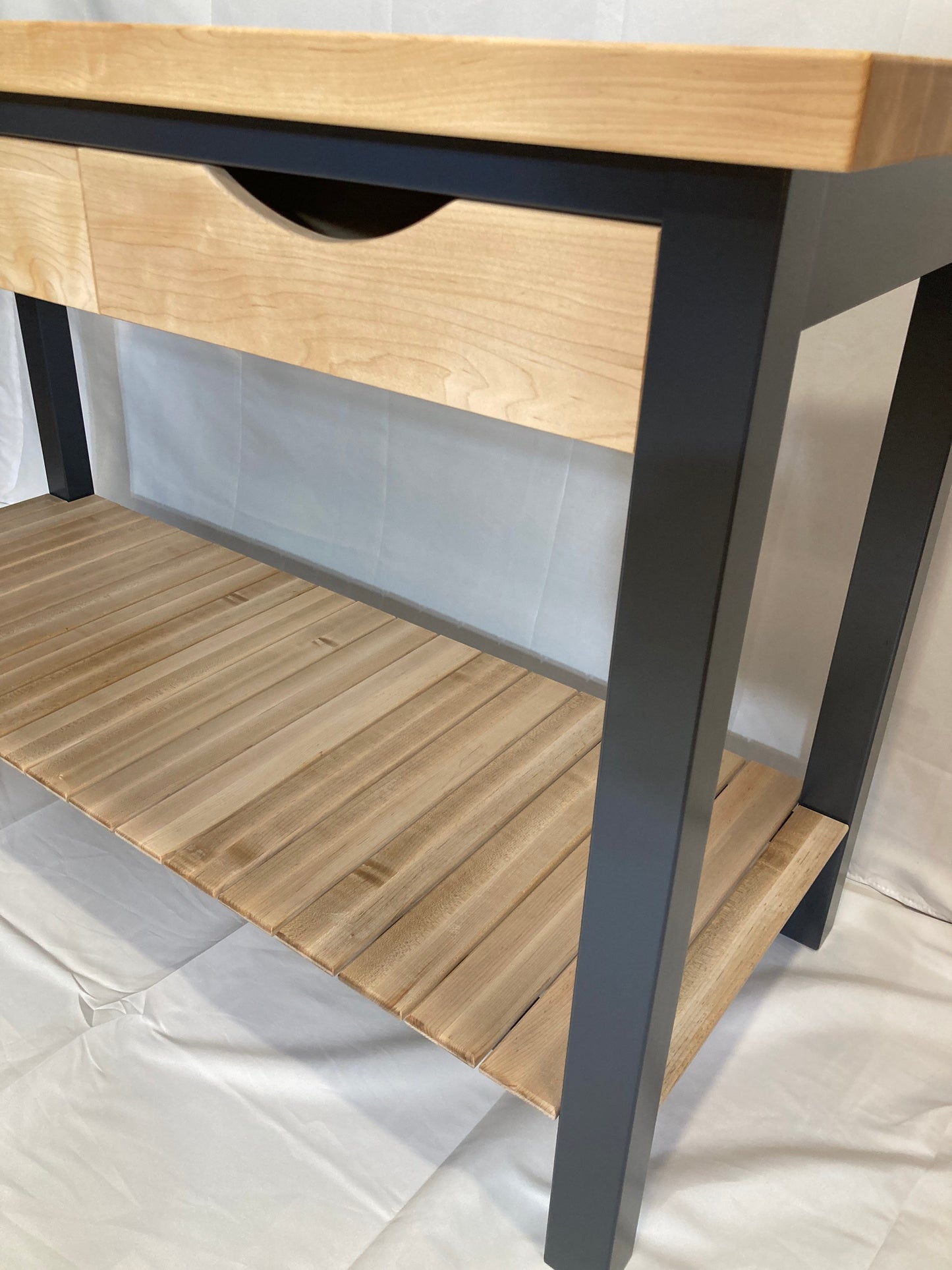 A modern kitchen island features a light maple wood top and a single drawer. The sleek dark blue frame provides a striking contrast. A lower shelf, also made of light maple wood, offers additional storage space. The clean lines and simple design make this kitchen island a perfect addition to any kitchen.