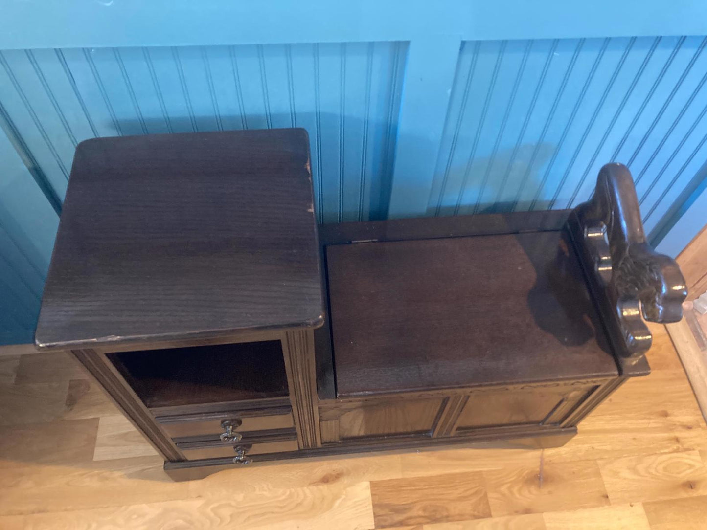 Dark brown wooden telephone table with a built-in seat and storage drawers. The table features carved details on the seat back and three drawers underneath the top surface. The top is a dark, rich brown color, and the overall style is traditional and classic.