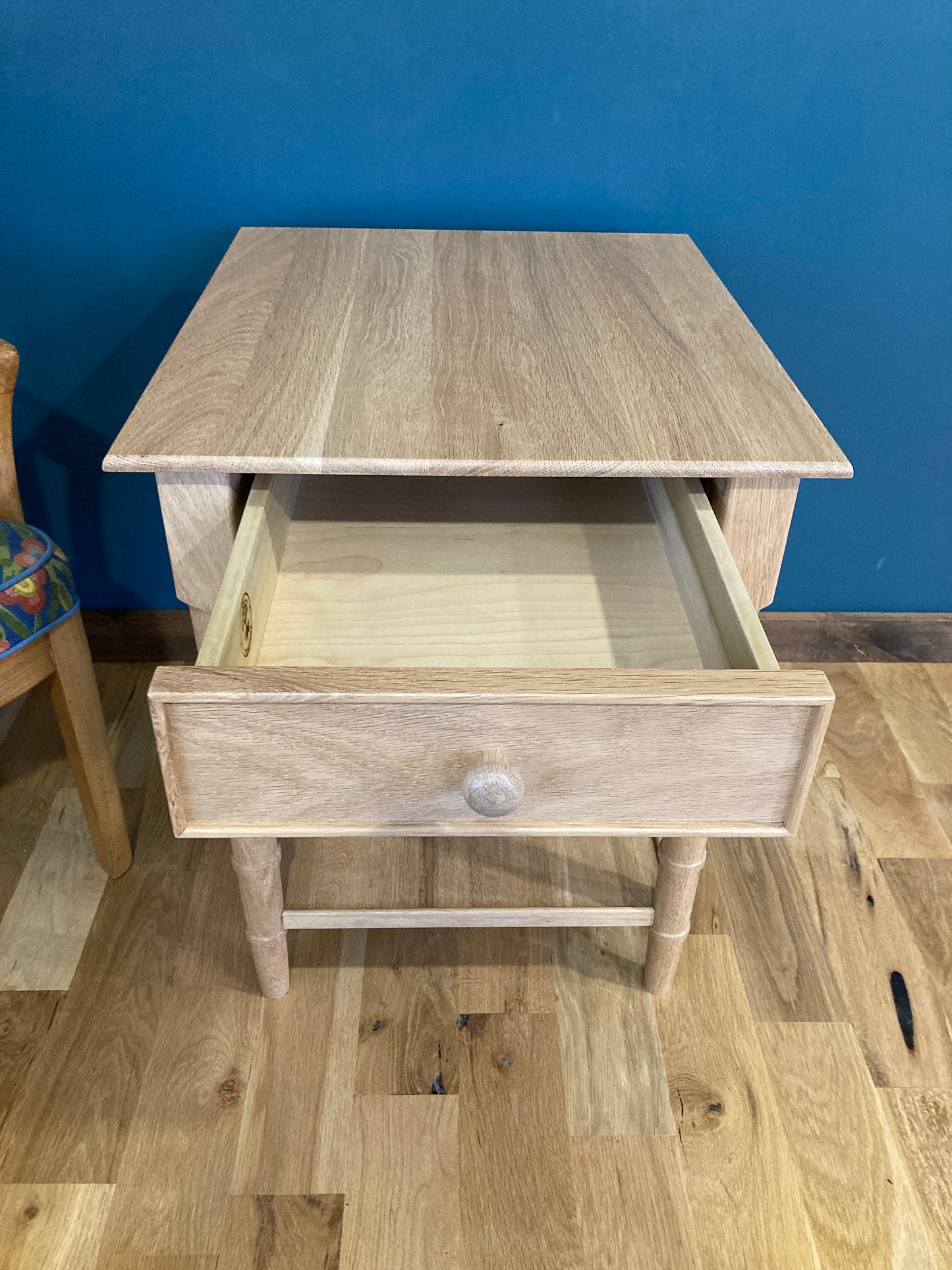 A light wood end table with a single drawer and four legs. The drawer is open and the inside is visible. The table is on a wood floor.