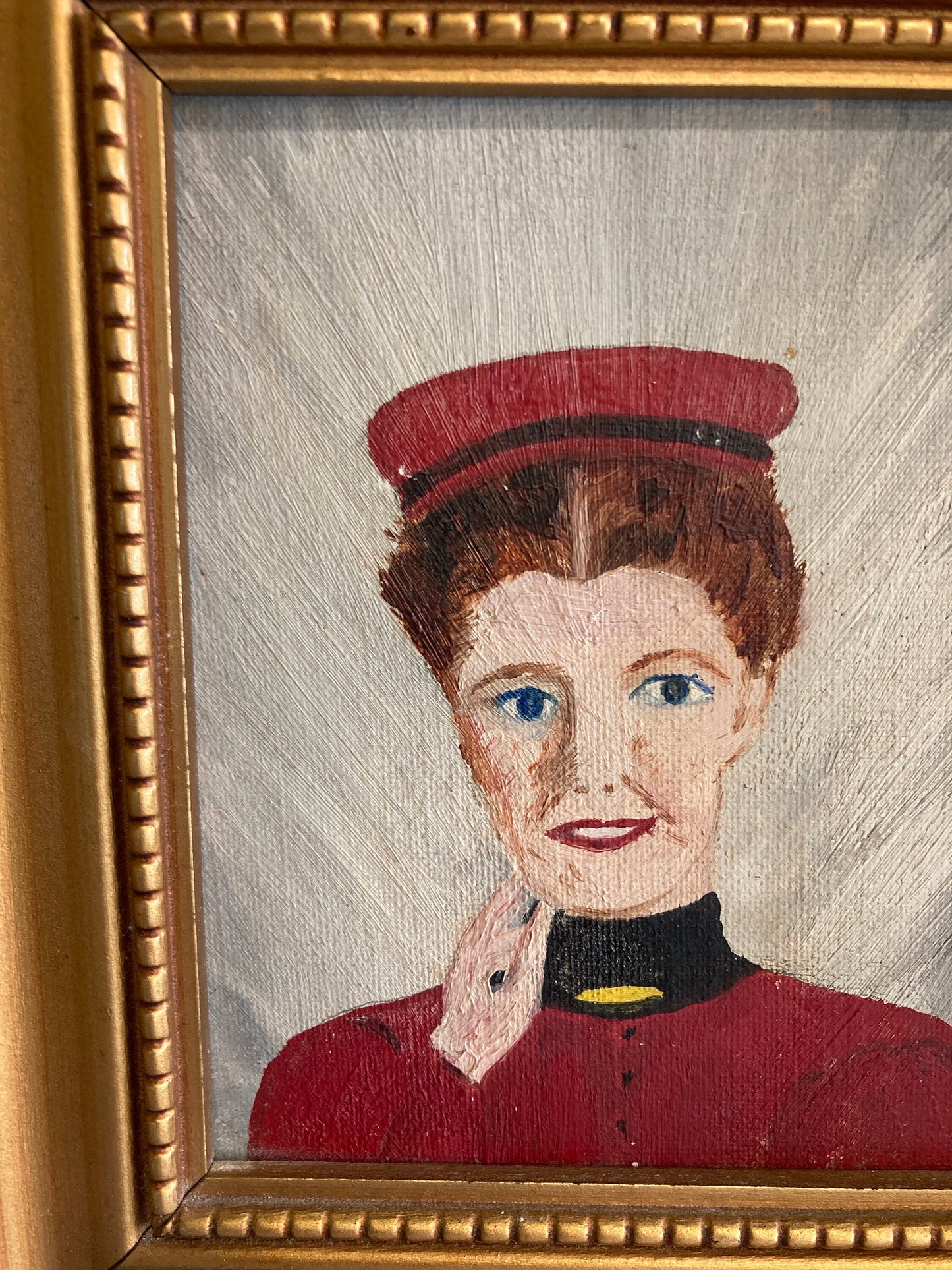 A framed painting of a person with red hair wearing a red hat and a red jacket with a black collar and a yellow trim.