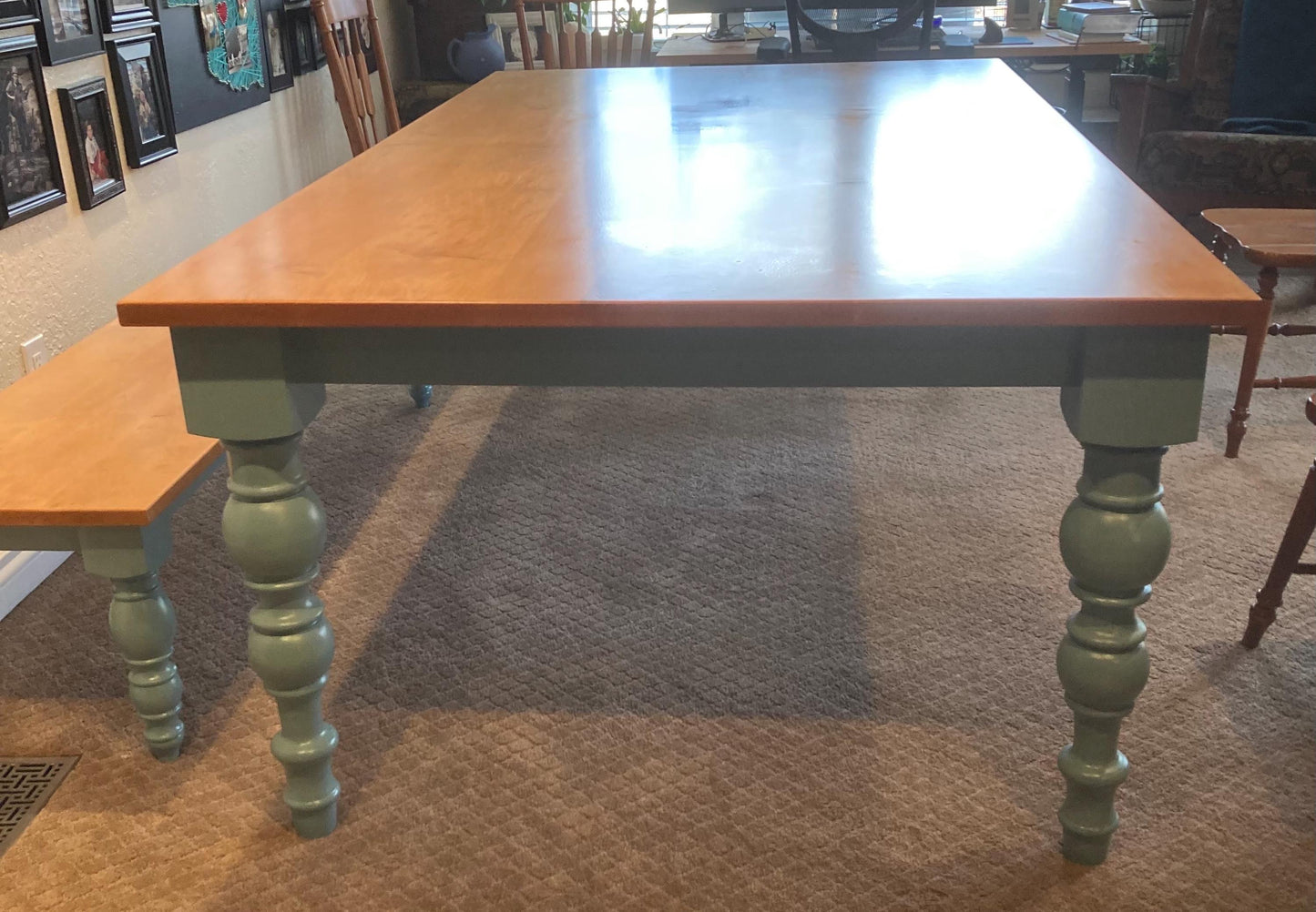 A light wood table with a light wood bench. The table has four legs with a turned design and is painted a light blue color. The table and bench are on a brown carpet.