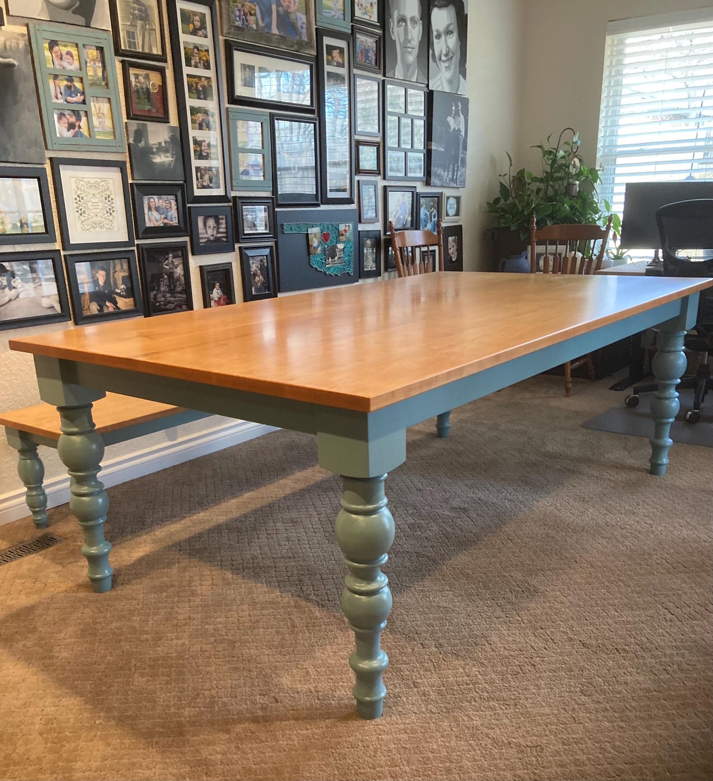 A light maple wood table with a light blue base and turned legs. The table has a light wood top and is sitting on a light brown carpet.