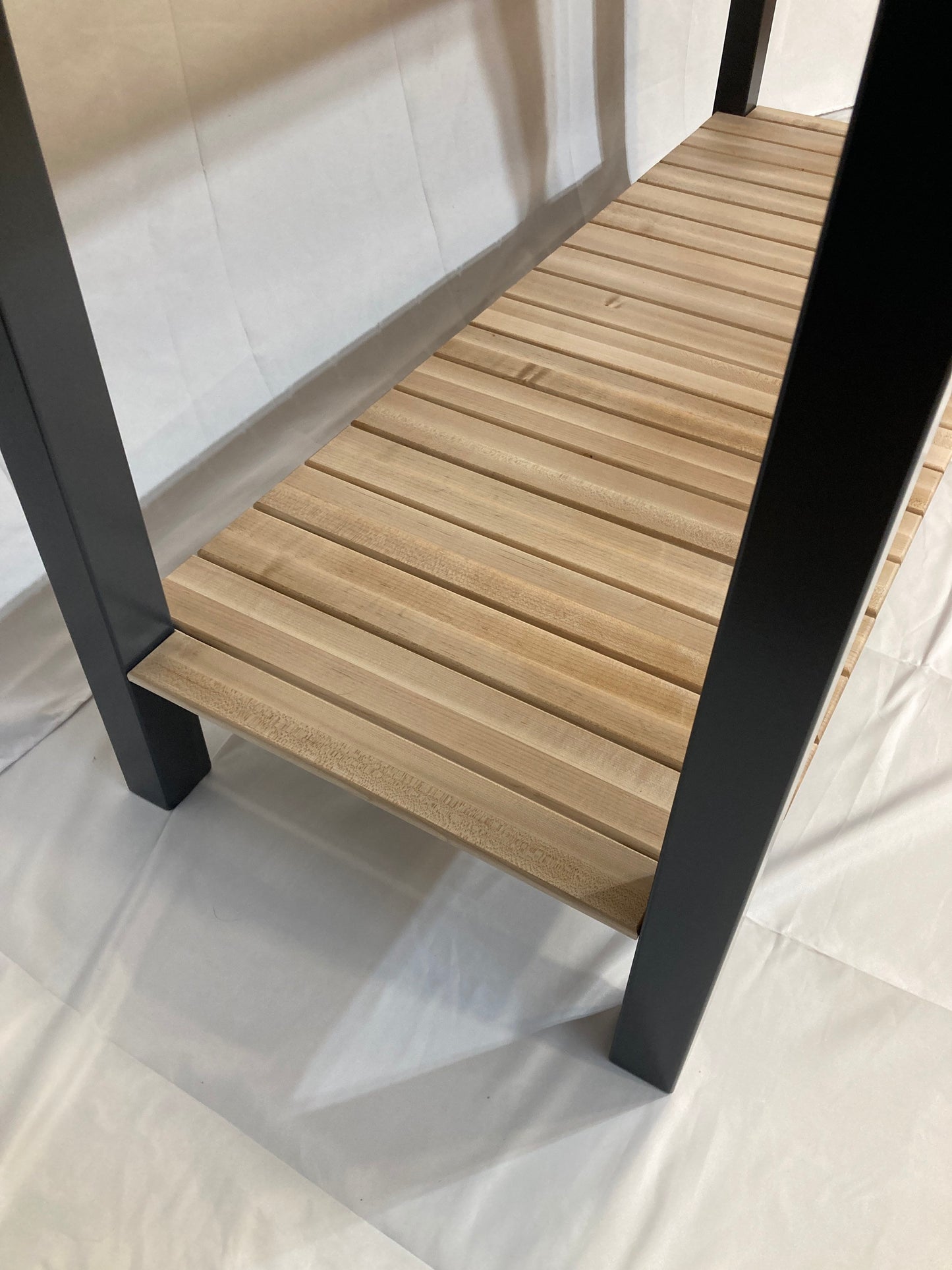 Close-up view of a wooden shelf with blue legs. The shelf is made of light-colored wood planks, arranged horizontally, creating a slatted look. The blue legs are square and sturdy, providing support for the shelf. The shelf is part of a butcher block kitchen island. The overall style is modern and minimalist, with a clean and simple design. The image is well-lit, showcasing the texture and color of the wood and legs.