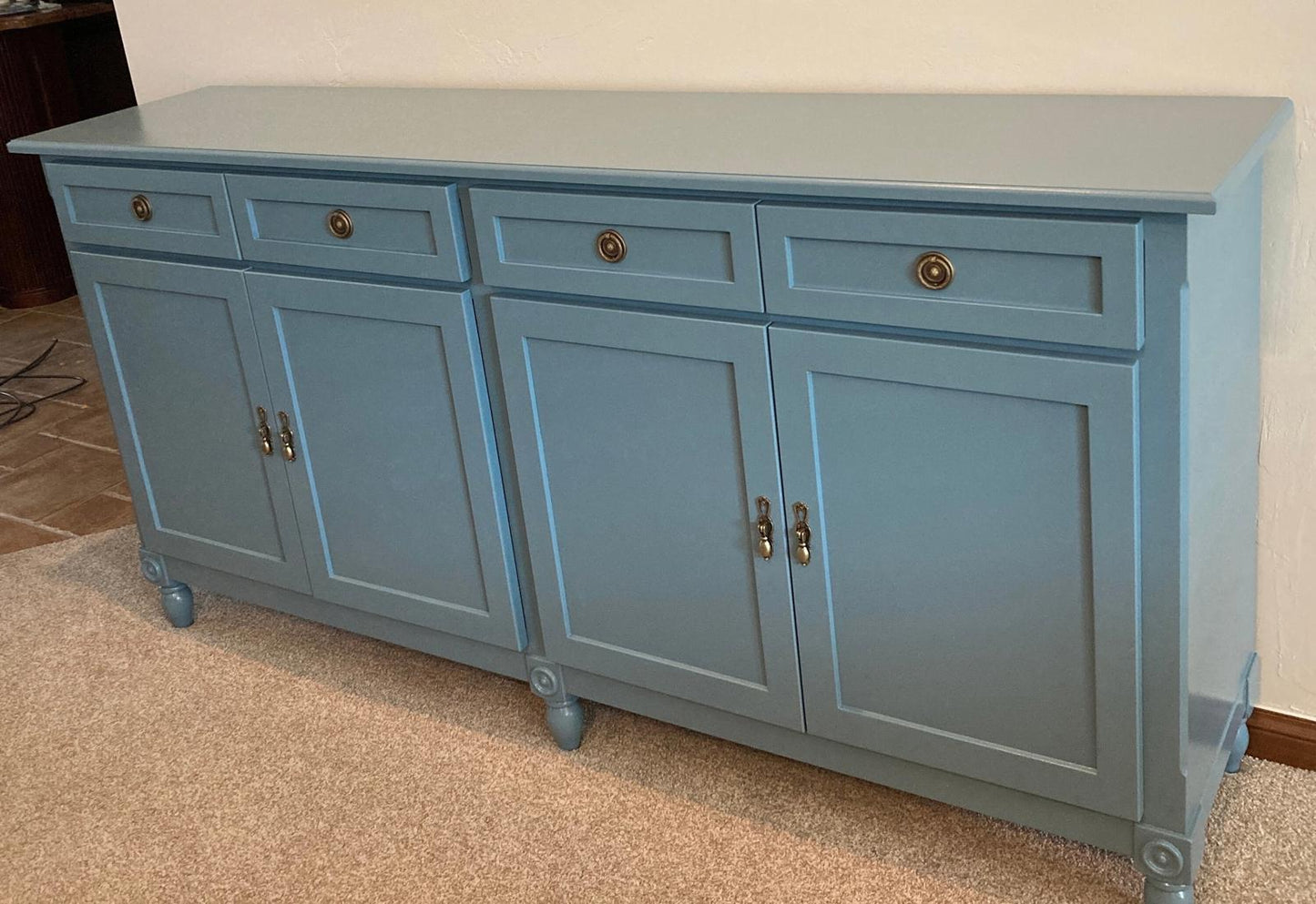 A light blue wooden cabinet with four doors and four drawers. The cabinet has brass handles and sits on four hand turned legs.