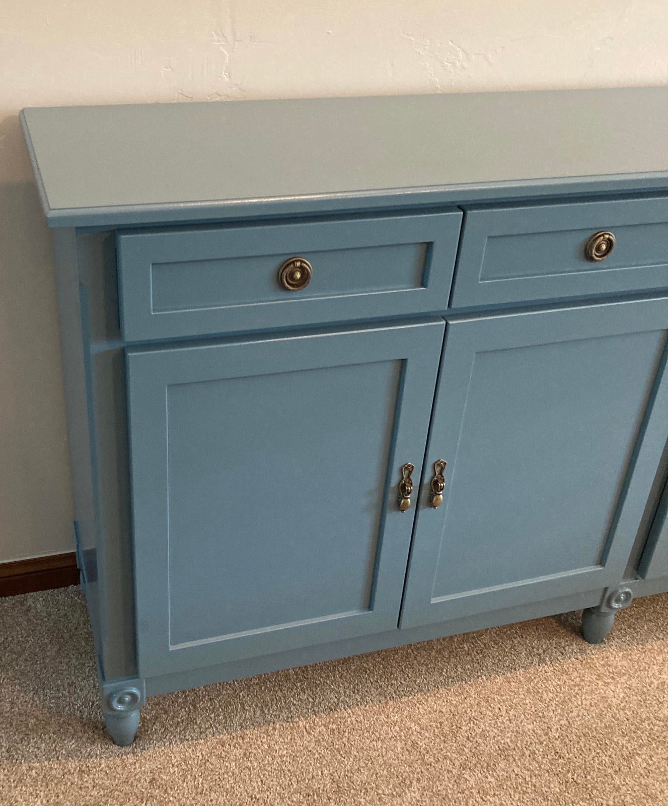 The left side focus of a blue wooden cabinets two drawers and two doors. The cabinet has brass hardware and sits on four legs.