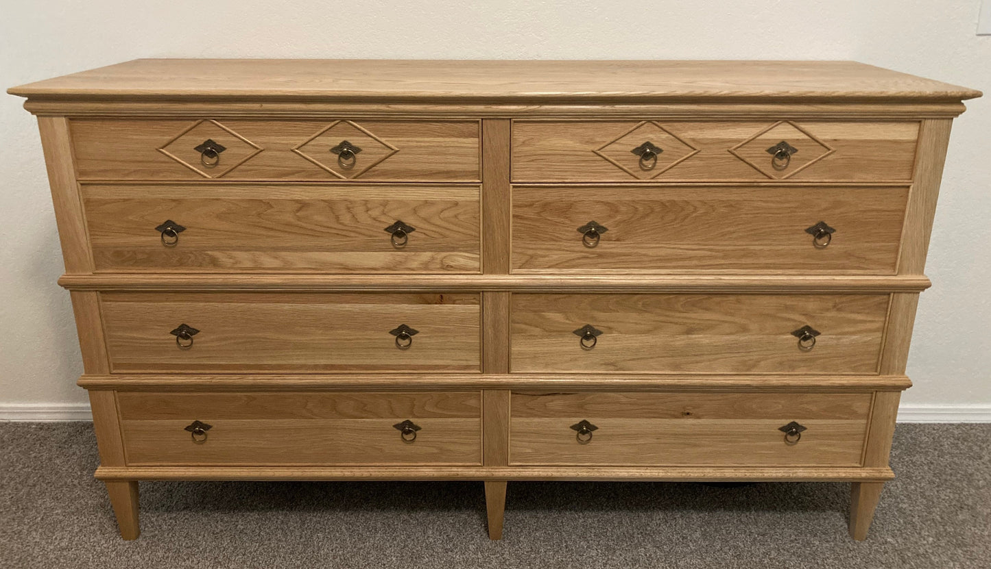 An eight-drawer dresser made of light wood with a natural finish. The dresser has eight drawers with brass knobs and a diamond-shaped design on the top two drawers