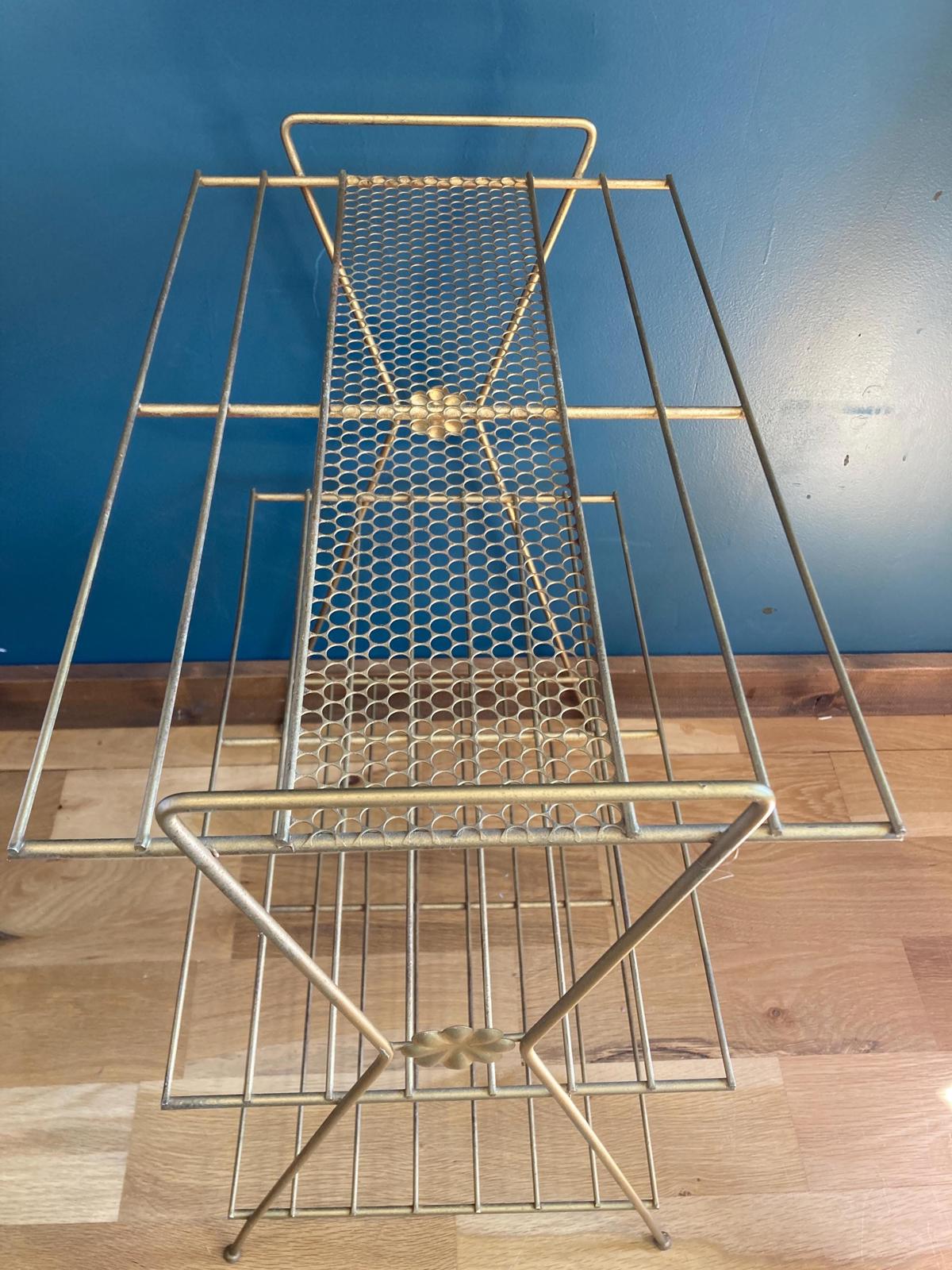 Gold metal three-tiered shelf with a geometric design. Each shelf is made of gold wire mesh. The shelf has a modern mid-century style. The shelf is ideal for displaying decorative items or storing small objects.
