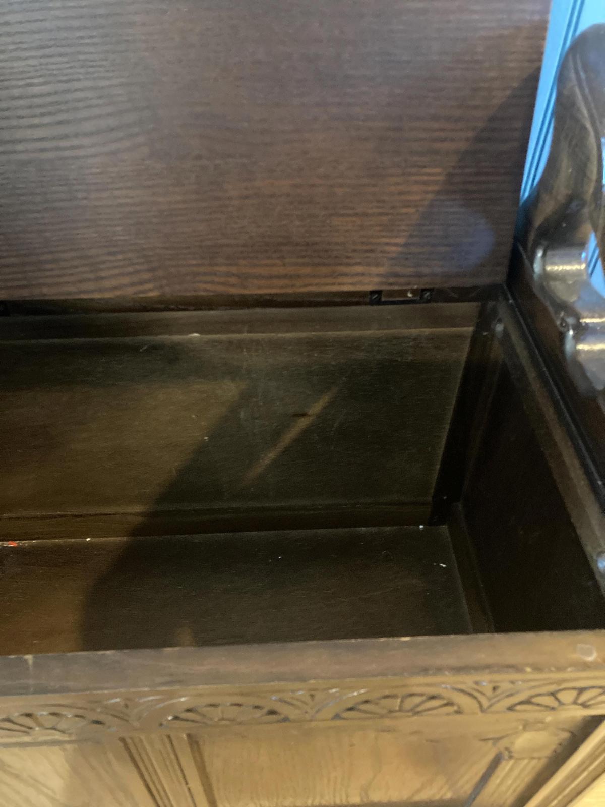 A dark brown wooden storage chest with carved details. The chest has a hinged lid that opens to reveal an empty interior. The wood grain is visible, and the carving is intricate. The chest appears to be antique or vintage, and is made of high-quality wood. The chest is a functional piece of furniture that could be used for storage or as a decorative element.