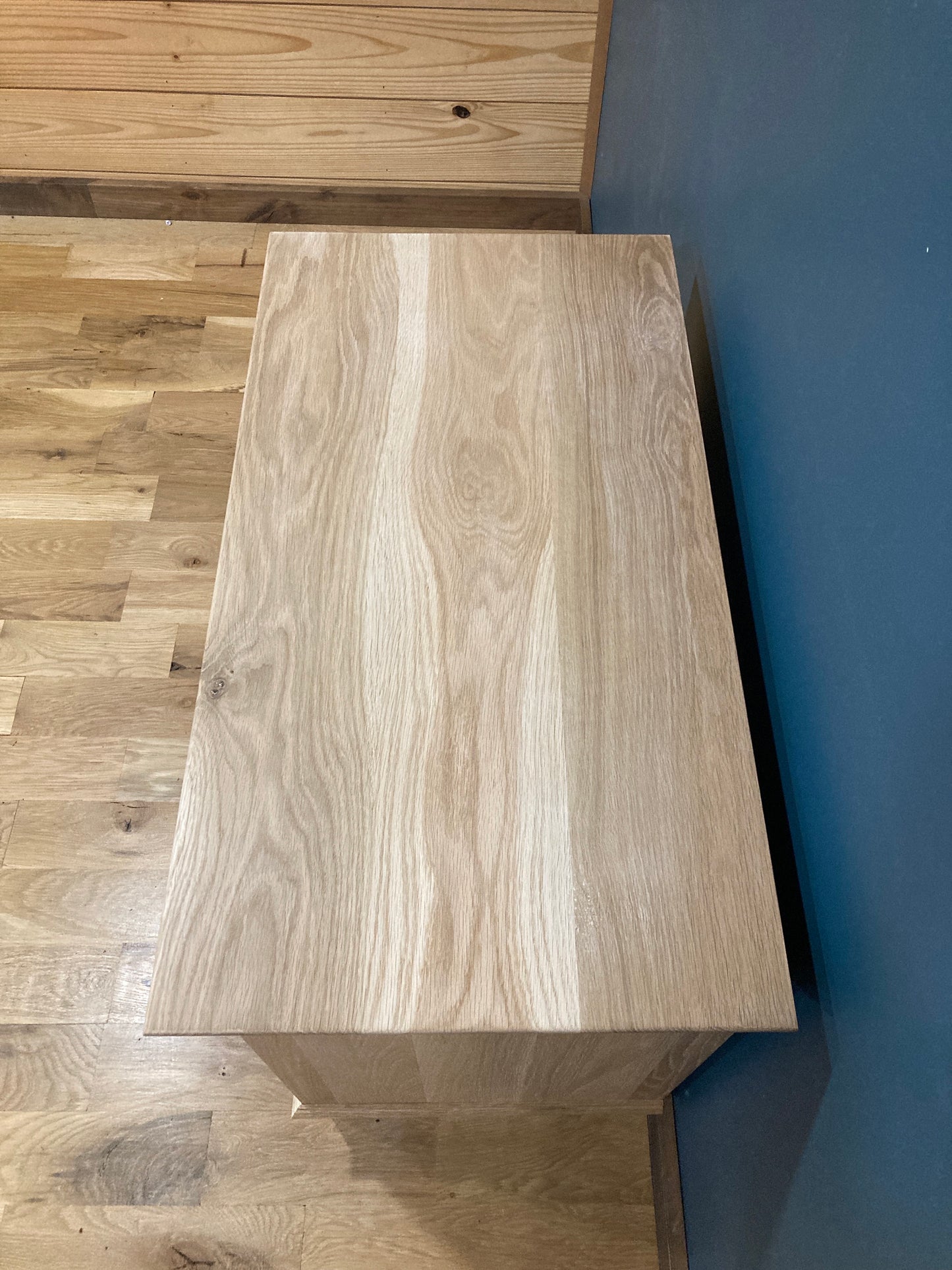 A light brown wooden nightstand with a top made of wood with a grain pattern. The cabinet is sitting on a wooden floor.