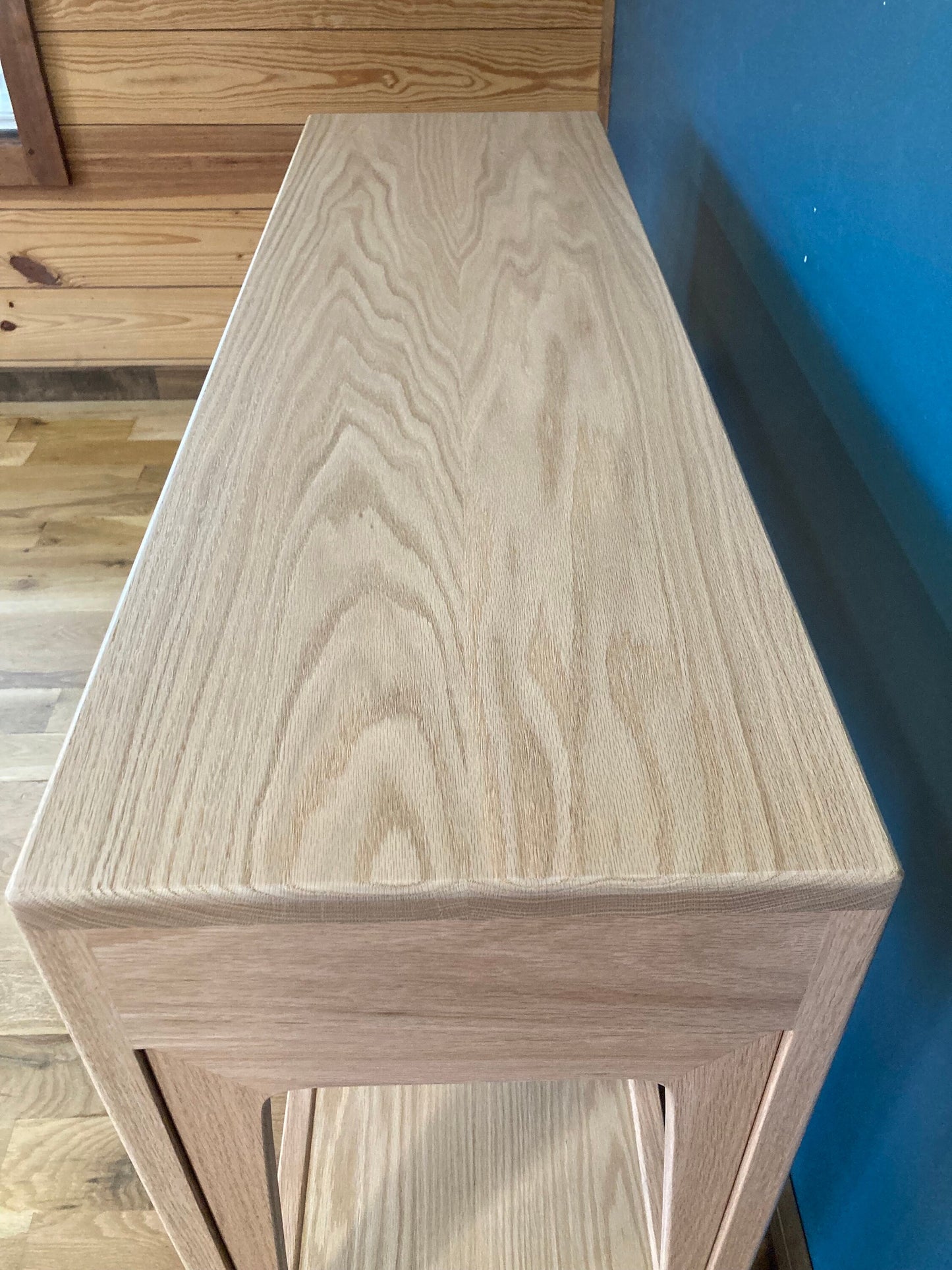  A light wood console table with a curved top and a shelf. The table has a natural wood finish and is made of solid wood.