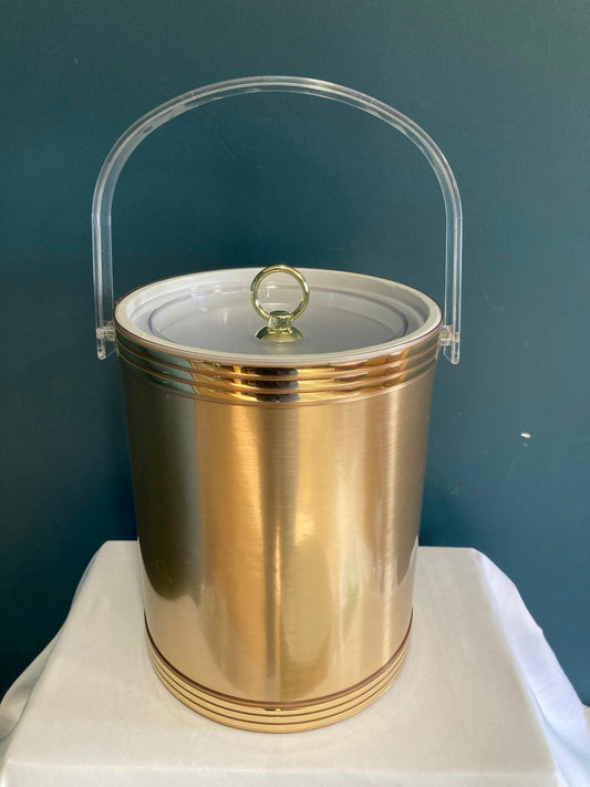 Gold cylindrical midcentury ice bucket with a clear cover on a blue background