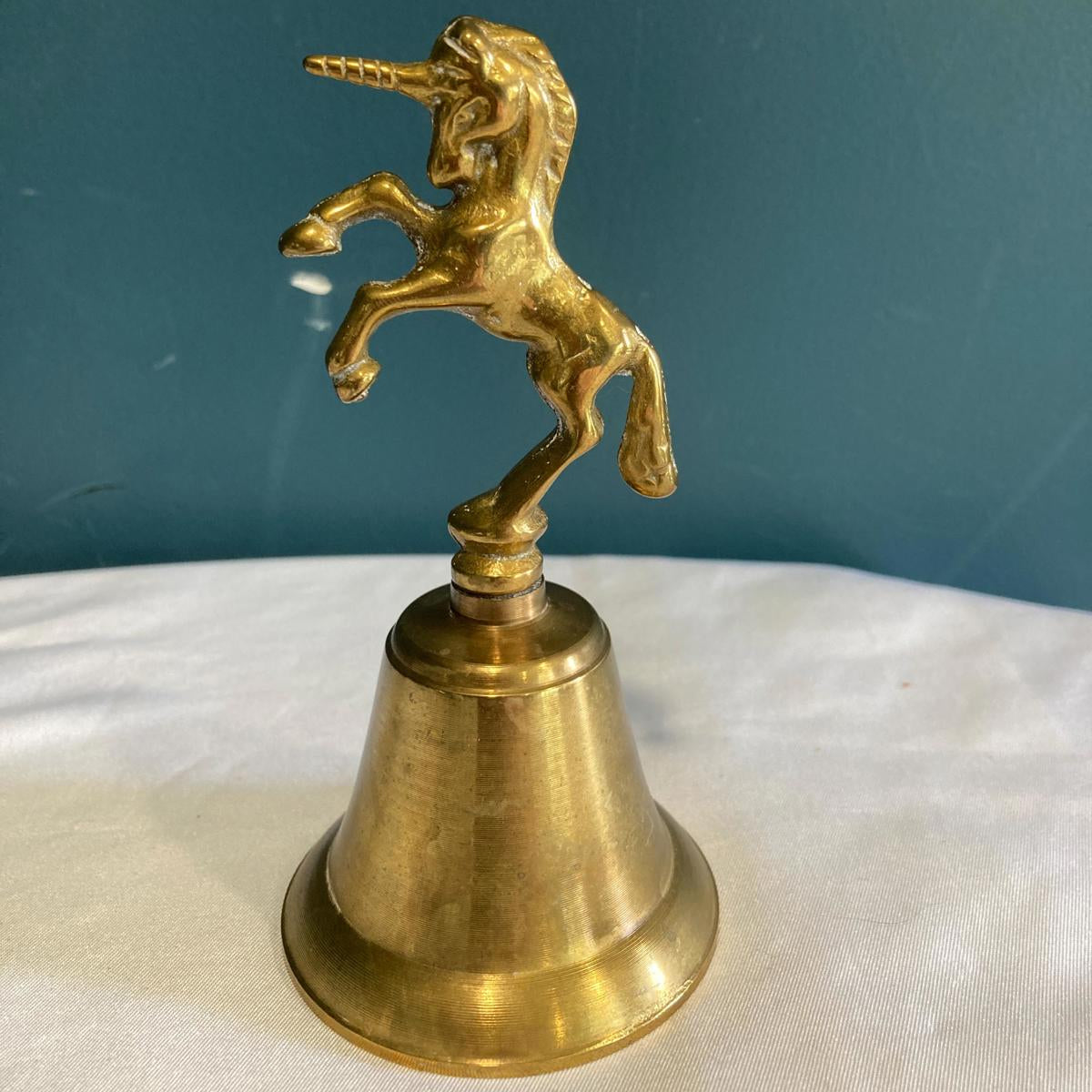 Brass bell with a unicorn figure on a white surface and blue background