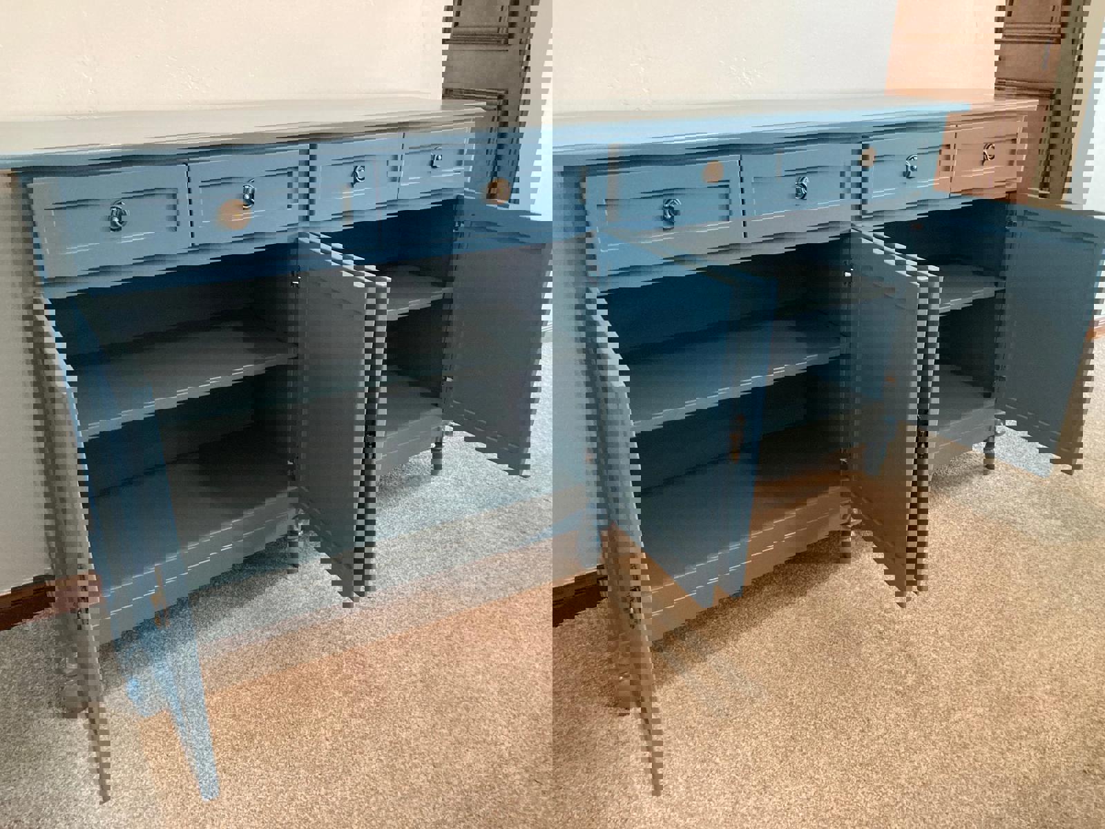A blue wooden cabinet with four drawers and four doors. The doors are open and reveal shelves inside. The cabinet has decorative legs and brass knobs.