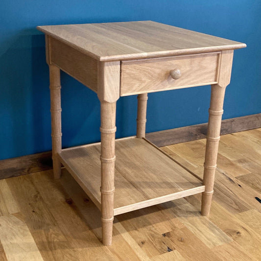 A light wood end table with a single drawer and a lower shelf. The table has turned faux bamboo legs and a simple design.