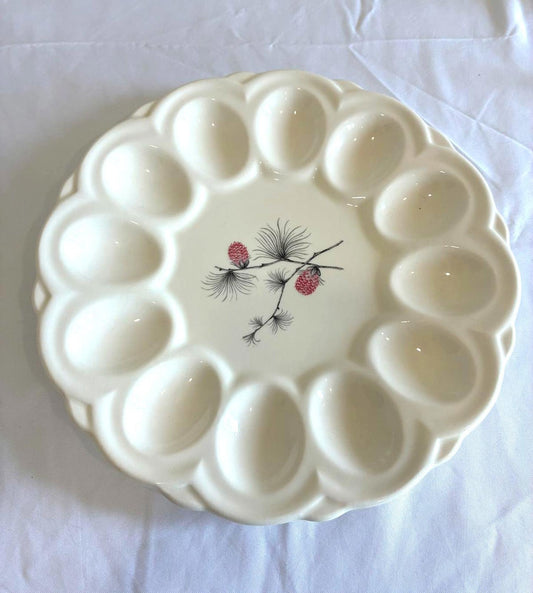 Vintage white deviled egg plate with pinecone design in center and individual egg wells arranged around the edge on white background