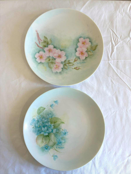 Two decorative plates with floral designs on a white fabric background