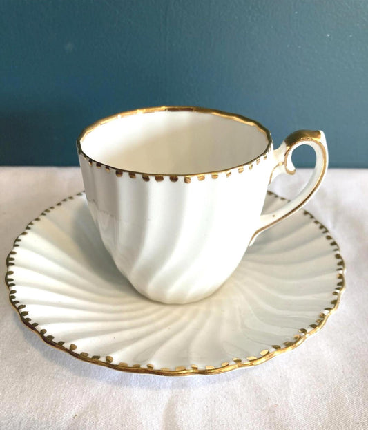White teacup and saucer with gold trim on a white surface with a blue background