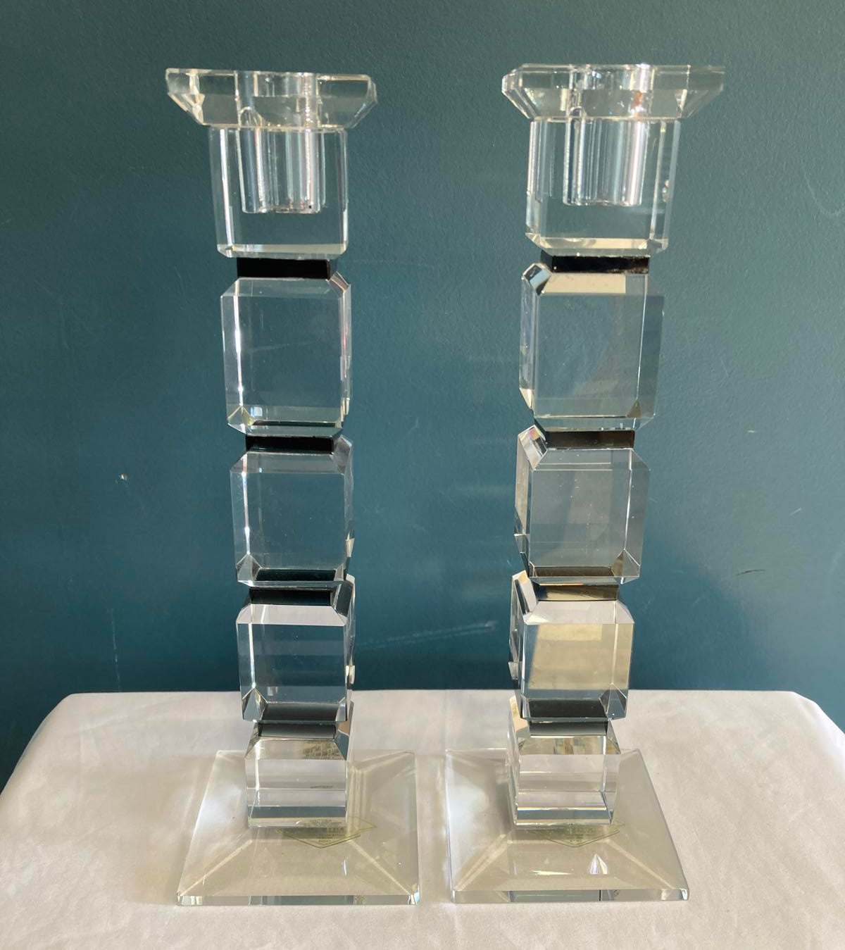 Crystal candlesticks with stacked cubes.  They are sitting on a white cloth in front of a teal wall. 