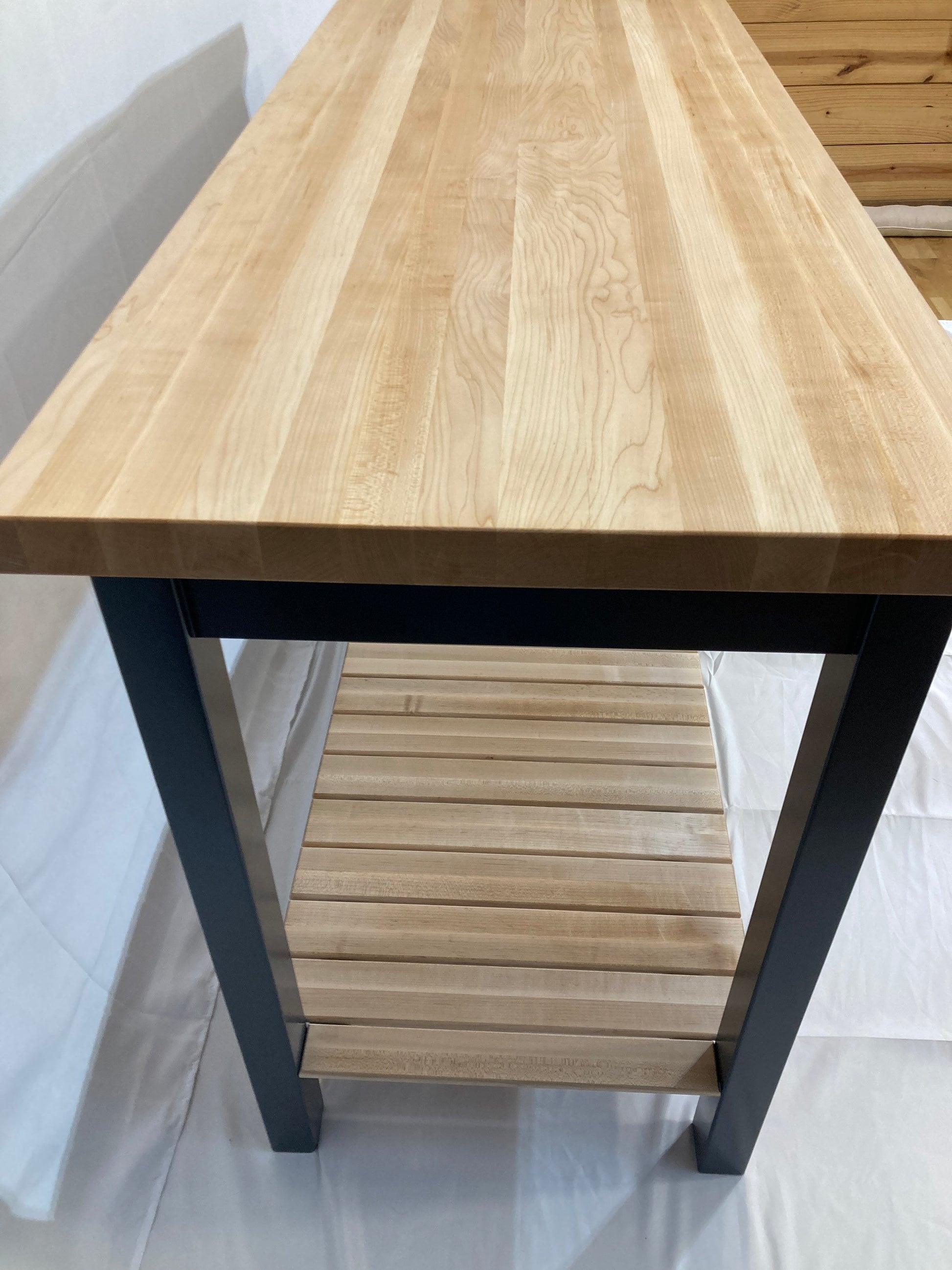  A kitchen island with a light maple butcher block countertop and a blue painted frame. The island features a lower shelf made of light maple wood slats. The island's clean lines and simple design create a modern aesthetic, suitable for various kitchen styles. The butcher block top is durable and easy to maintain, while the blue legs provide a sturdy and stylish base.  The open shelf offers convenient storage space.