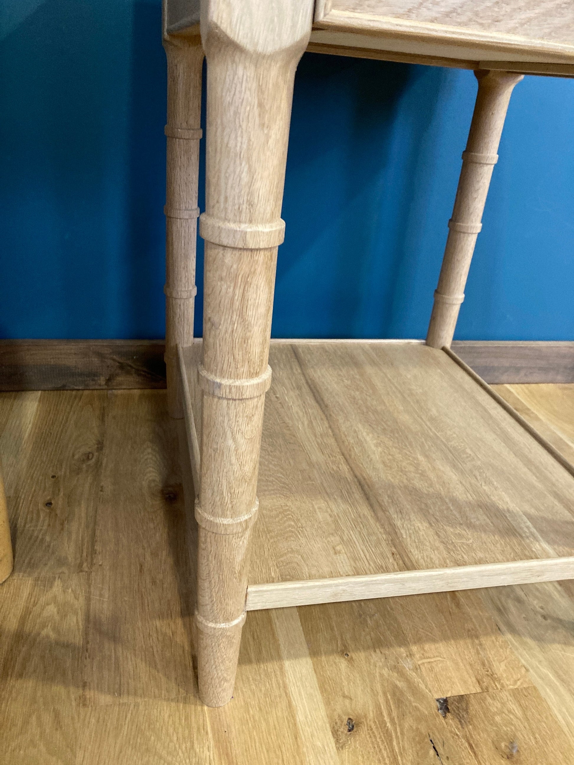 Close-up of a light wood end table with a single drawer and a lower shelf. The table has a simple design with turned faux bamboo legs and a rectangular top. The table is made of light wood and has a natural finish.