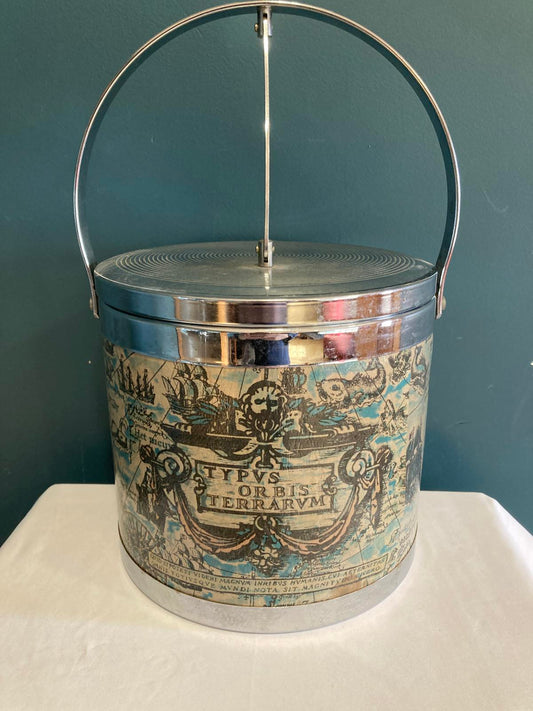 vintage ice bucket with old world map.  The ice bucket has an attached lid.  It is sitting on a white cloth in front of a teal background. 