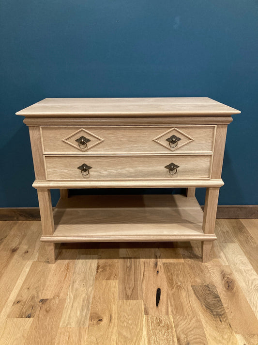 Custom hardwood nightstand with two drawers and a bottom shelf featuring diamond-patterned accents and vintage-style metal pulls, plus an open lower shelf, shown against a teal wall on hardwood flooring.