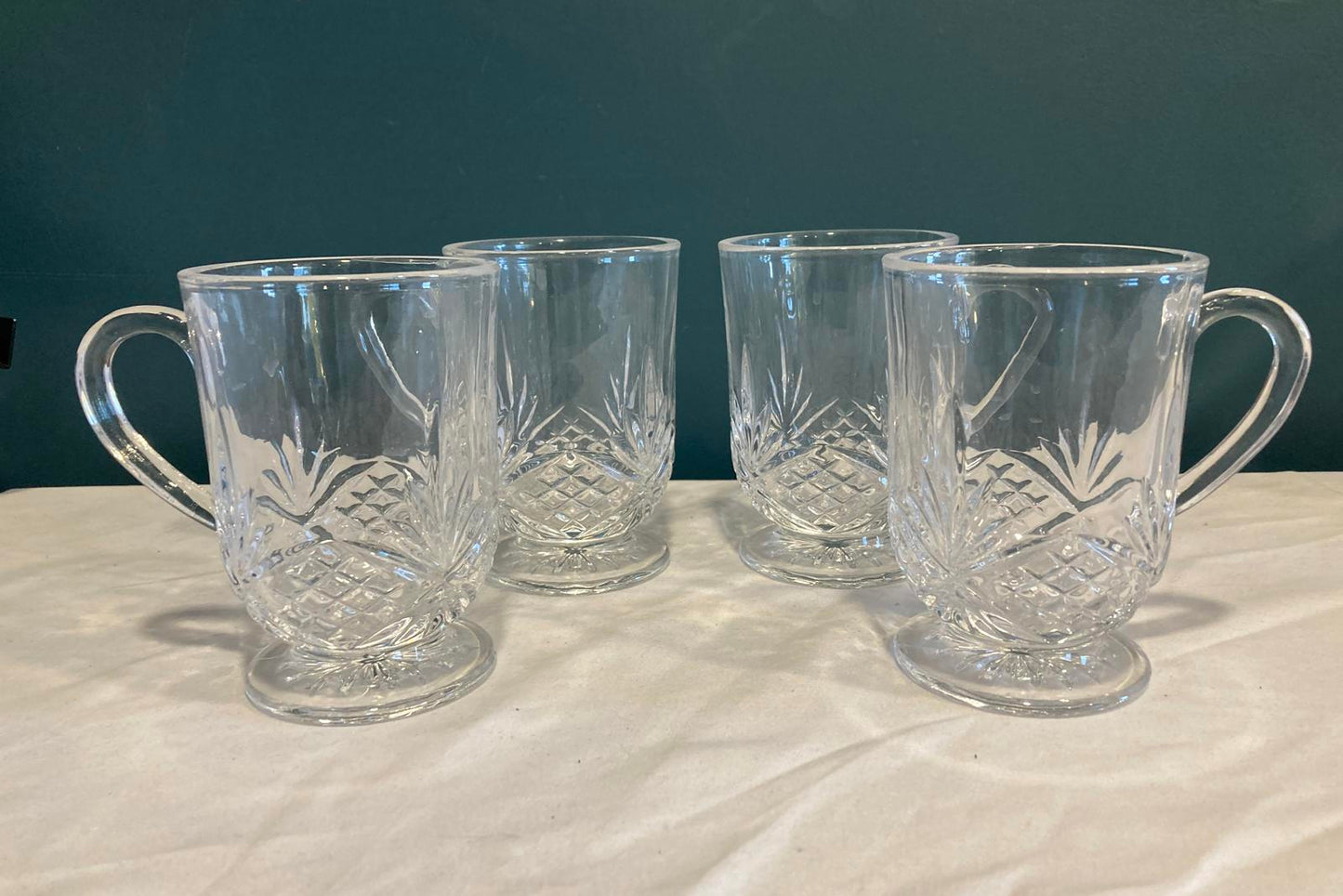 Set of four clear glass tumblers with handles on a white and blue gradient background