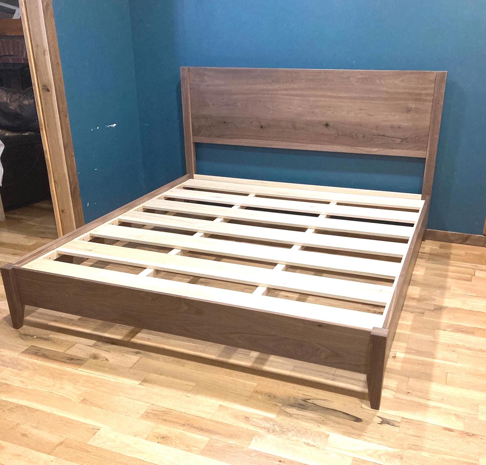 Solid walnut Wooden bed frame against a blue wall.  The bedframe has lighter colored wooden slats and is a simple design. 