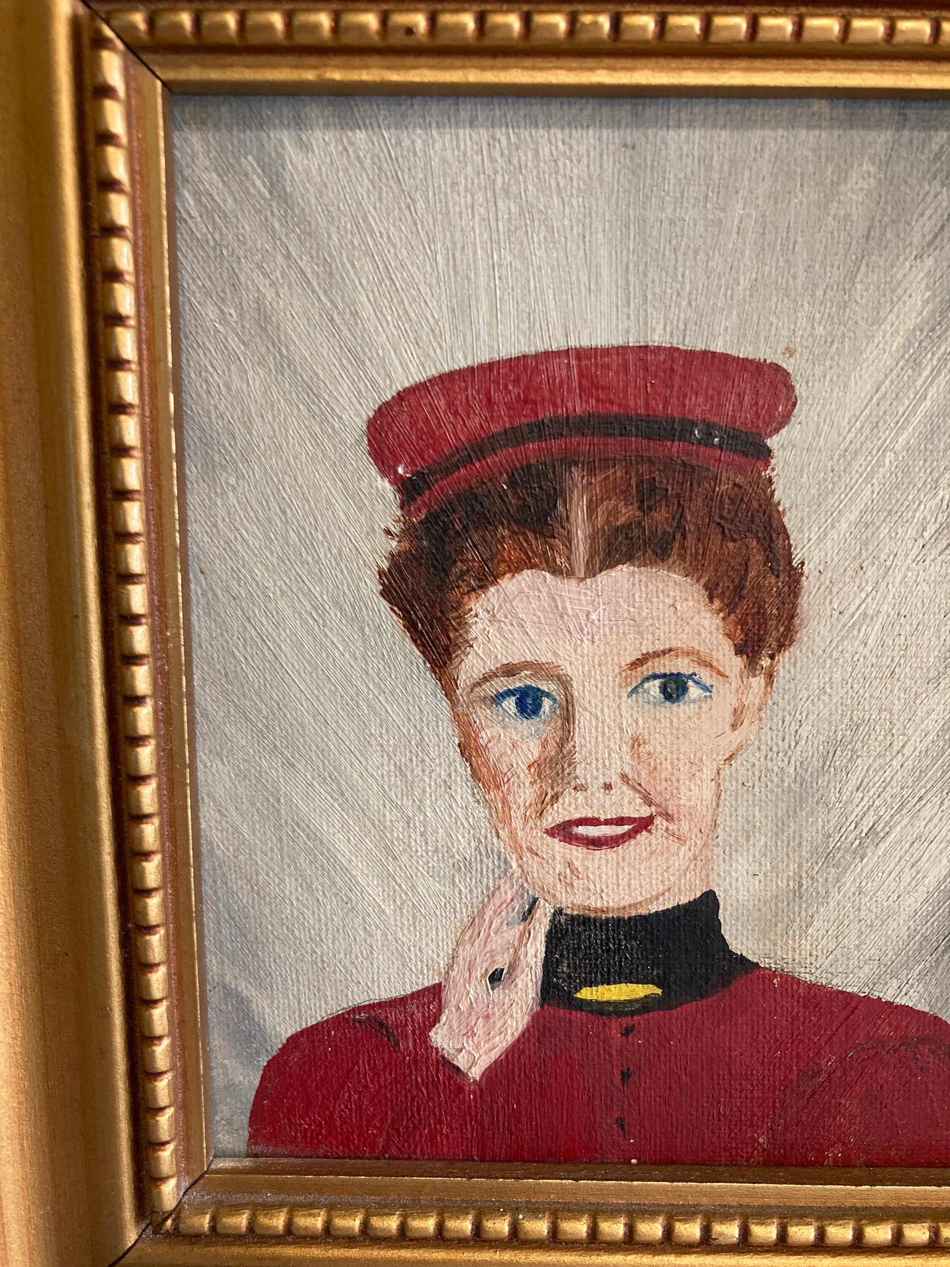 A framed painting of a person with red hair wearing a red hat and a red jacket with a black collar and a yellow trim.