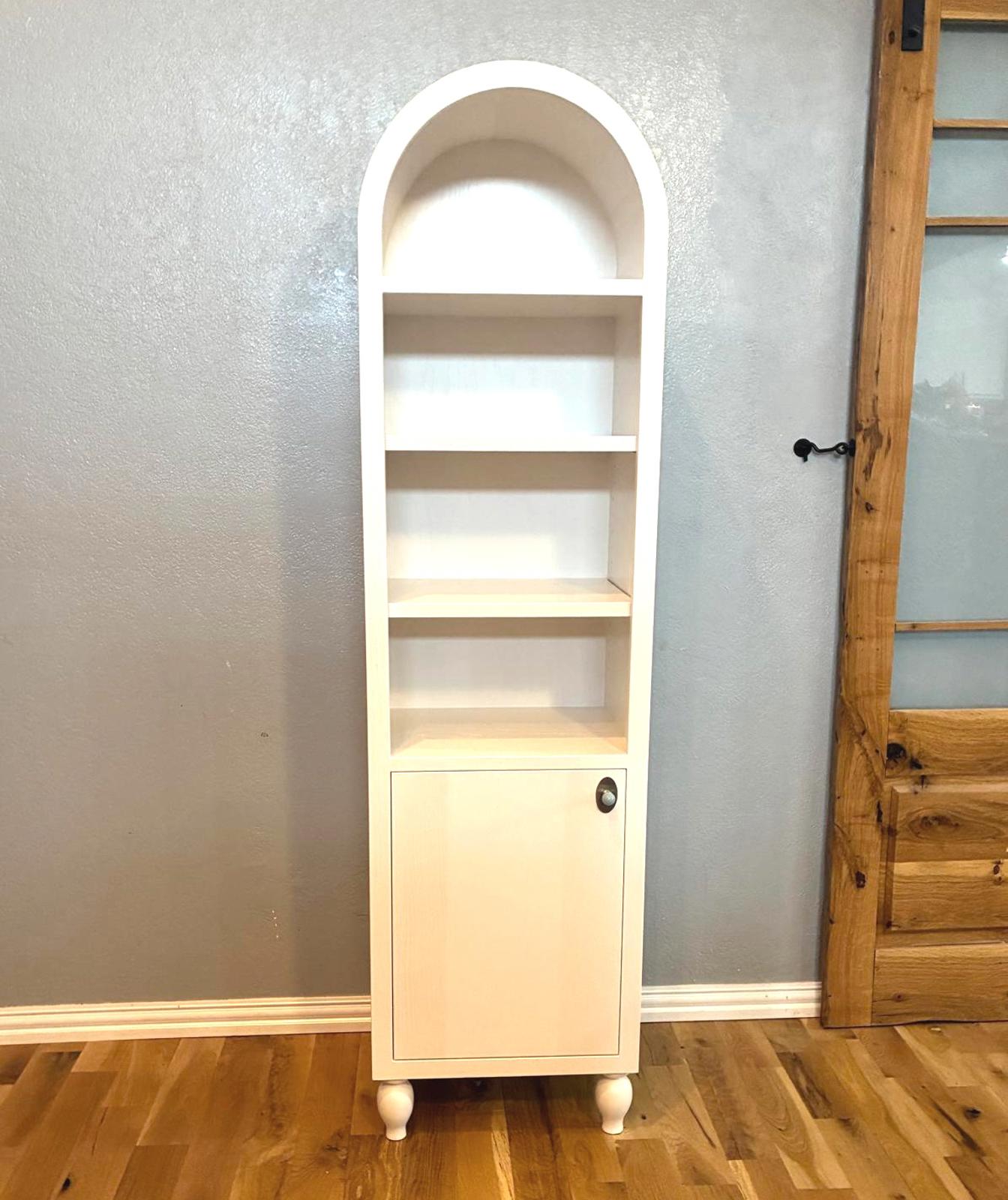 Handmade solid wood arched cabinet with three open shelves, lower door storage, and turned bun feet in a light natural finish against a neutral wall.