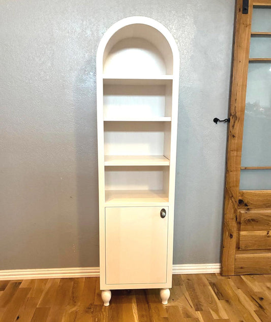 Handmade solid wood arched cabinet with three open shelves, lower door storage, and turned bun feet in a light natural finish against a neutral wall.