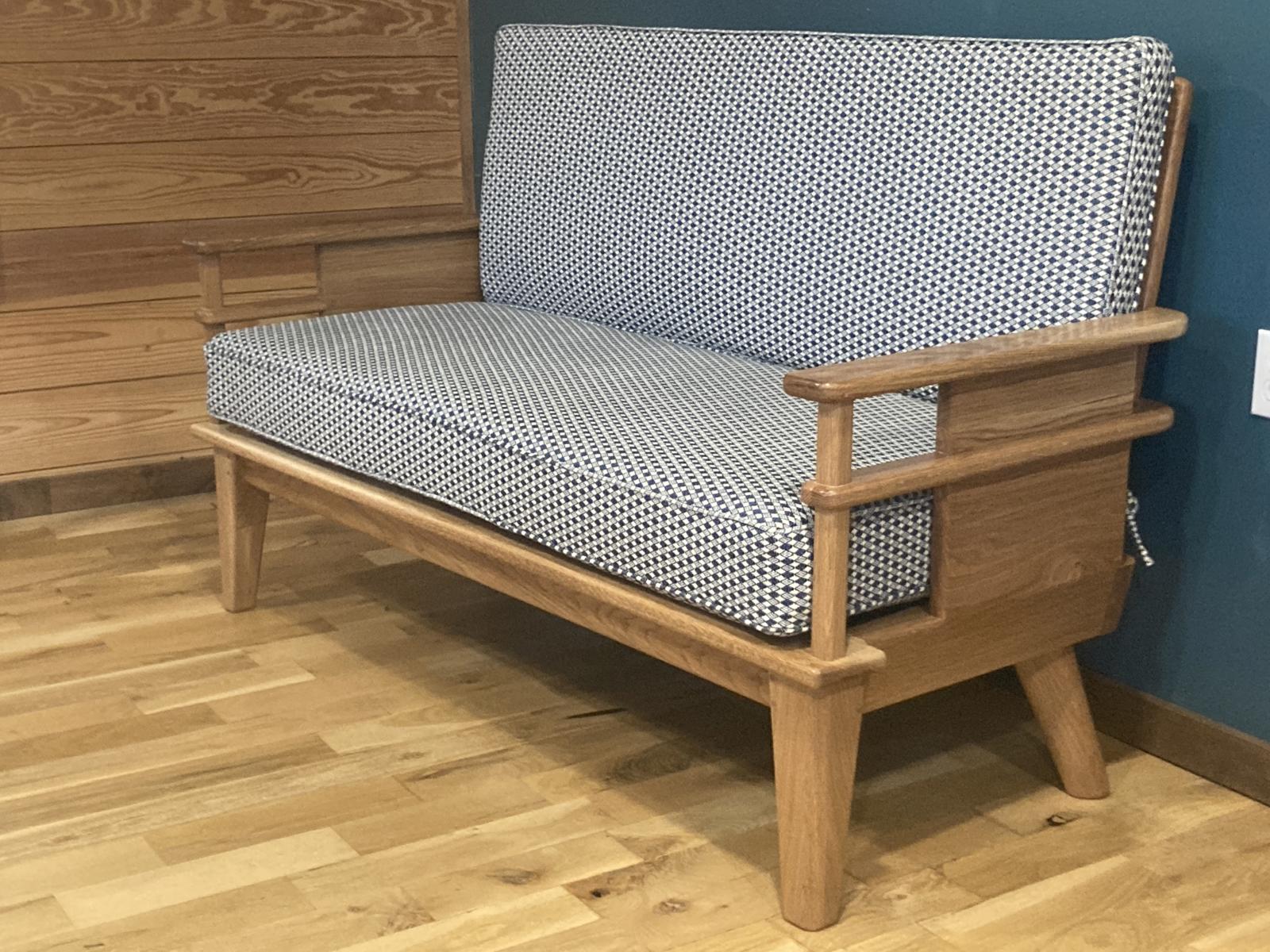 Handmade oak couch with a modern open-arm frame design, upholstered in blue and white houndstooth-style fabric, positioned on a wood floor next teal wall. The couch has wood arms and midcentury style legs. 