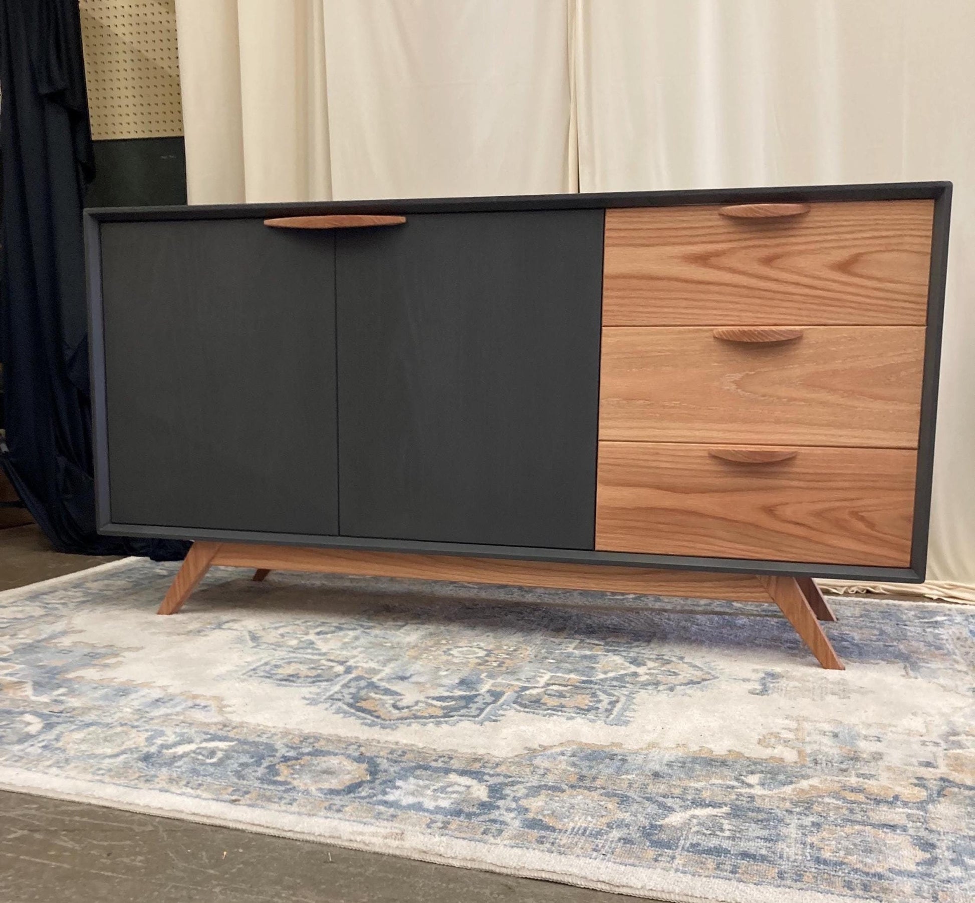 Mid-century modern sideboard with a matte gray frame and warm wood drawers and door handles, standing on angled legs