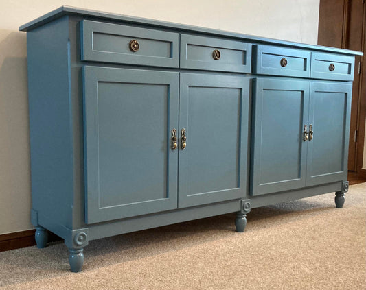 A blue wooden cabinet with four drawers and four doors. The cabinet has decorative legs and brass hardware. The cabinet is sitting on a carpet.