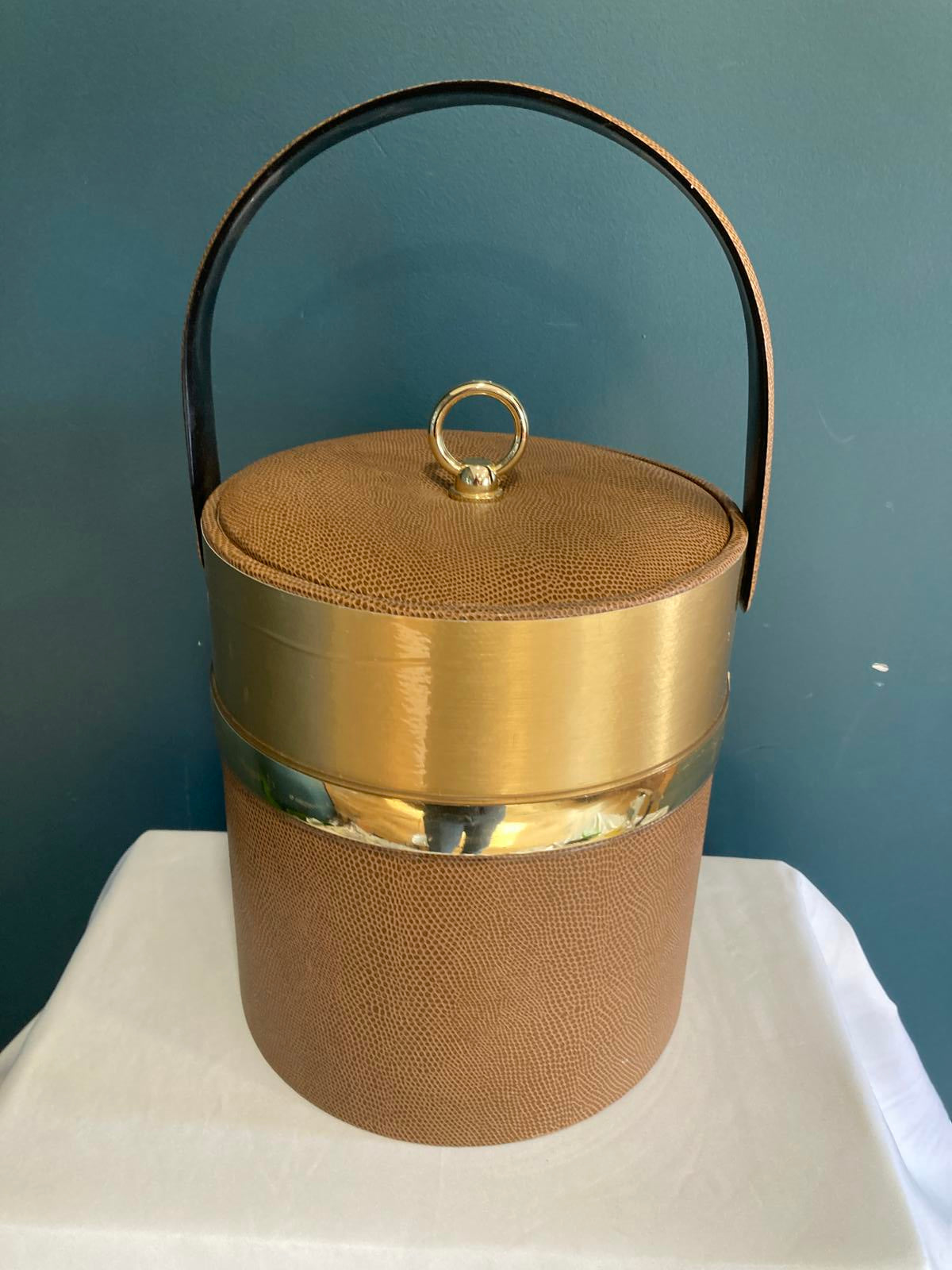Gold and brown cylindrical ice bucket with a handle on a dark surface