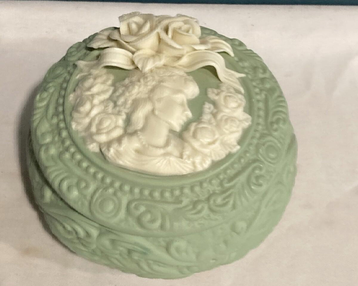 Decorative green ceramic trinket box with a woman's face and roses on a white surface.