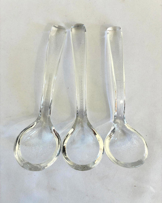 Three clear glass ladles with handles on a white background