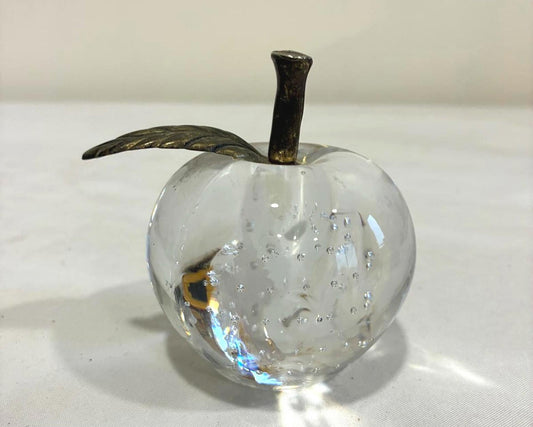 Clear glass apple with a brass stem on a white surface