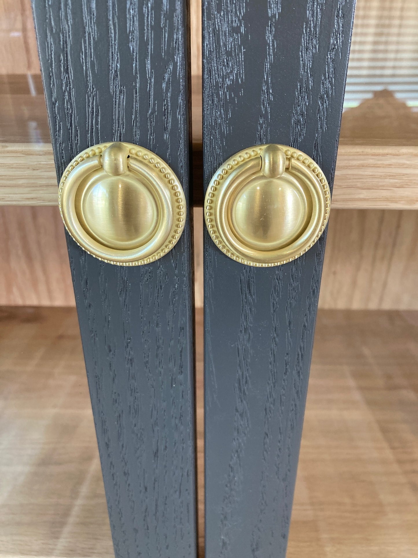 Two gray cabinet doors with gold ring-style handles with a beaded trim.