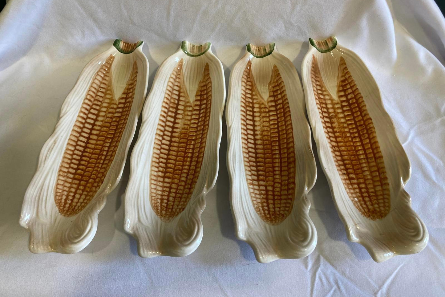 Four ceramic corn on the cob plates on a white background