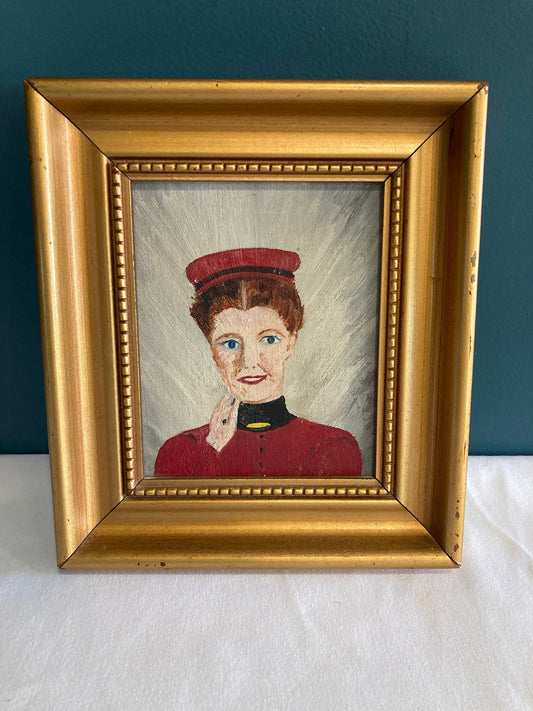 A framed painting of a woman wearing a red hat and a red dress with a black collar. The woman has her hand resting on the side of her face and is smiling and looking at the viewer.