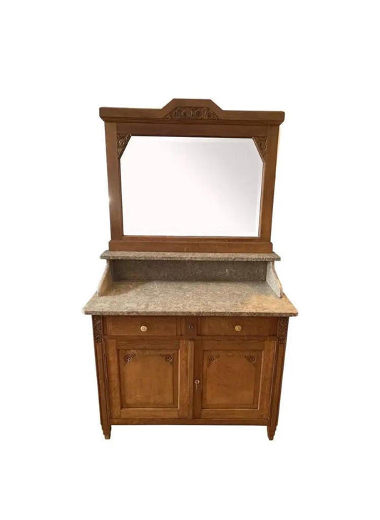 A wooden sideboard with a marble top and a mirror. The sideboard has two drawers and two doors. The mirror is framed in wood and has a decorative carved top.