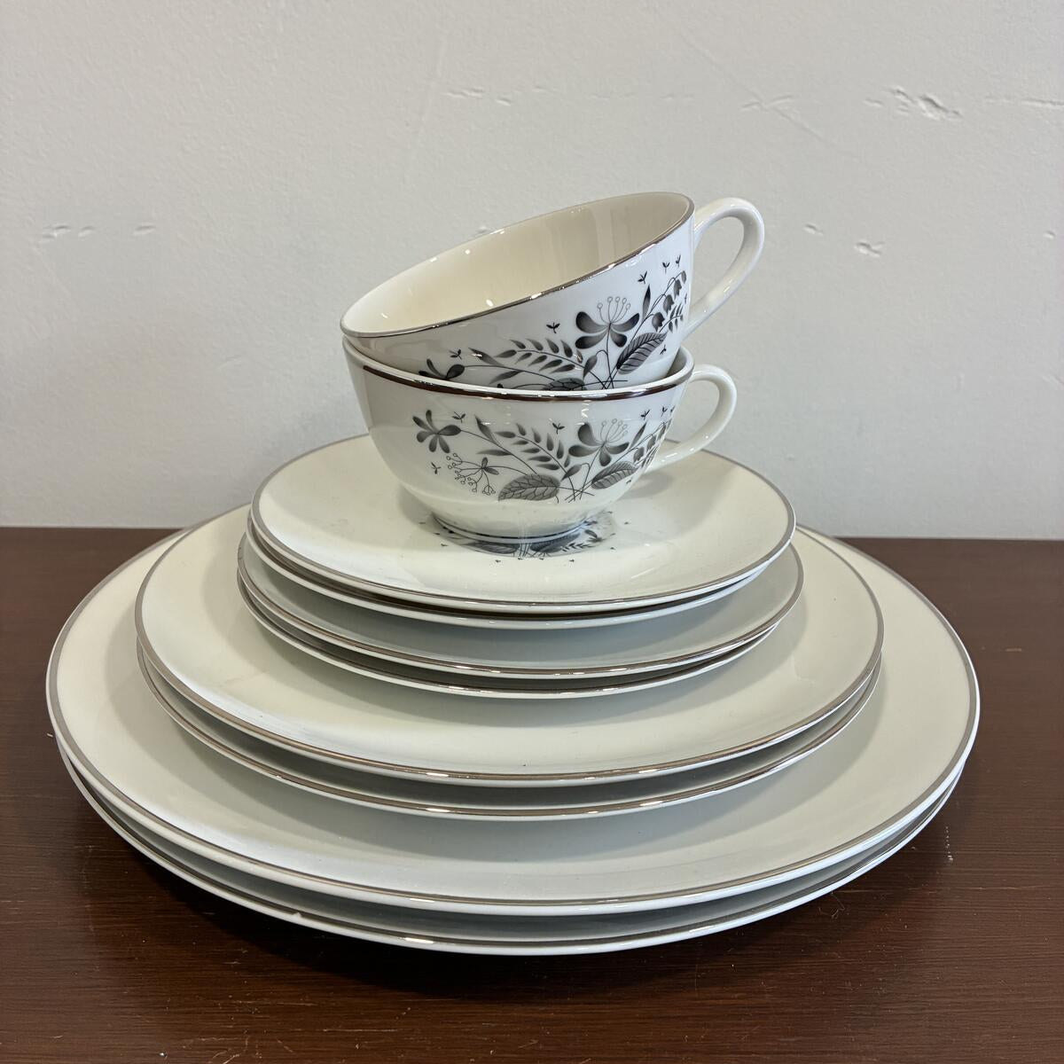 Vintage Royal Jackson Parisienne dinnerware set with black floral pattern including plates, cups, and saucers stacked on a wooden surface