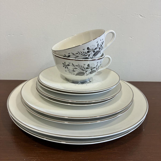 Vintage Royal Jackson Parisienne dinnerware set with black floral pattern including plates, cups, and saucers stacked on a wooden surface