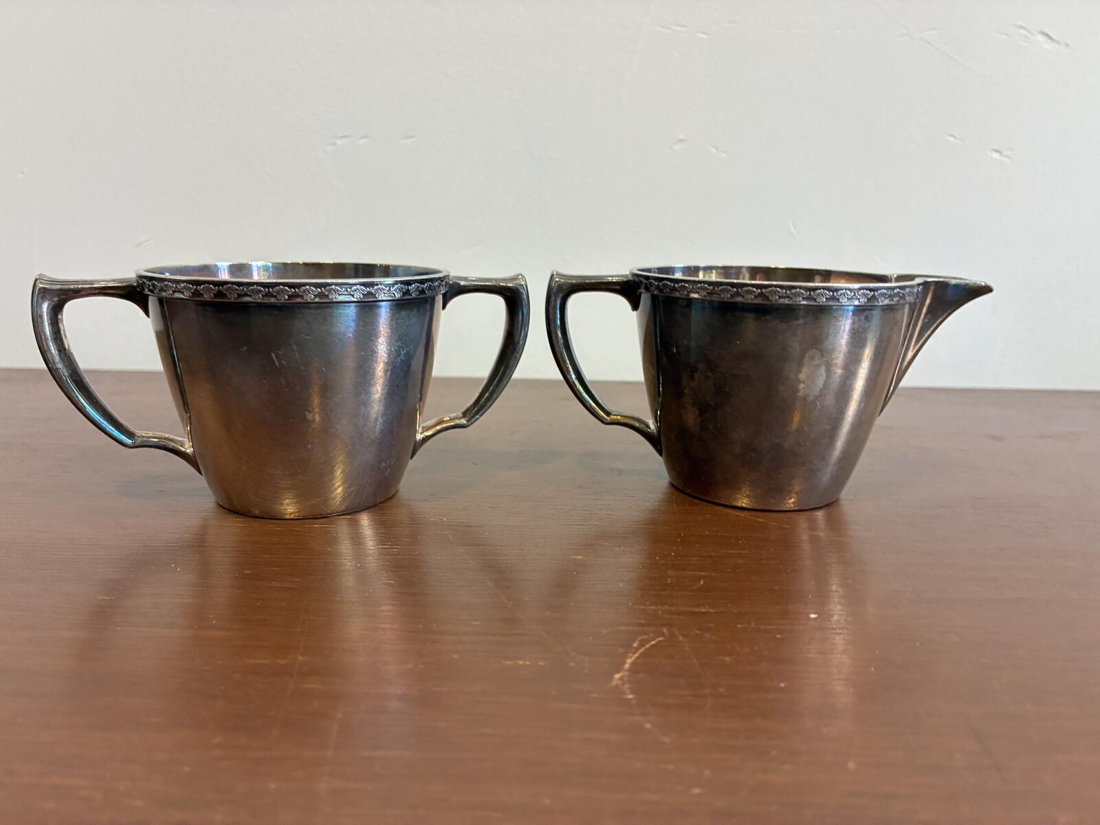 Silverplate sugar bowl and creamer with handles on a wooden surface.